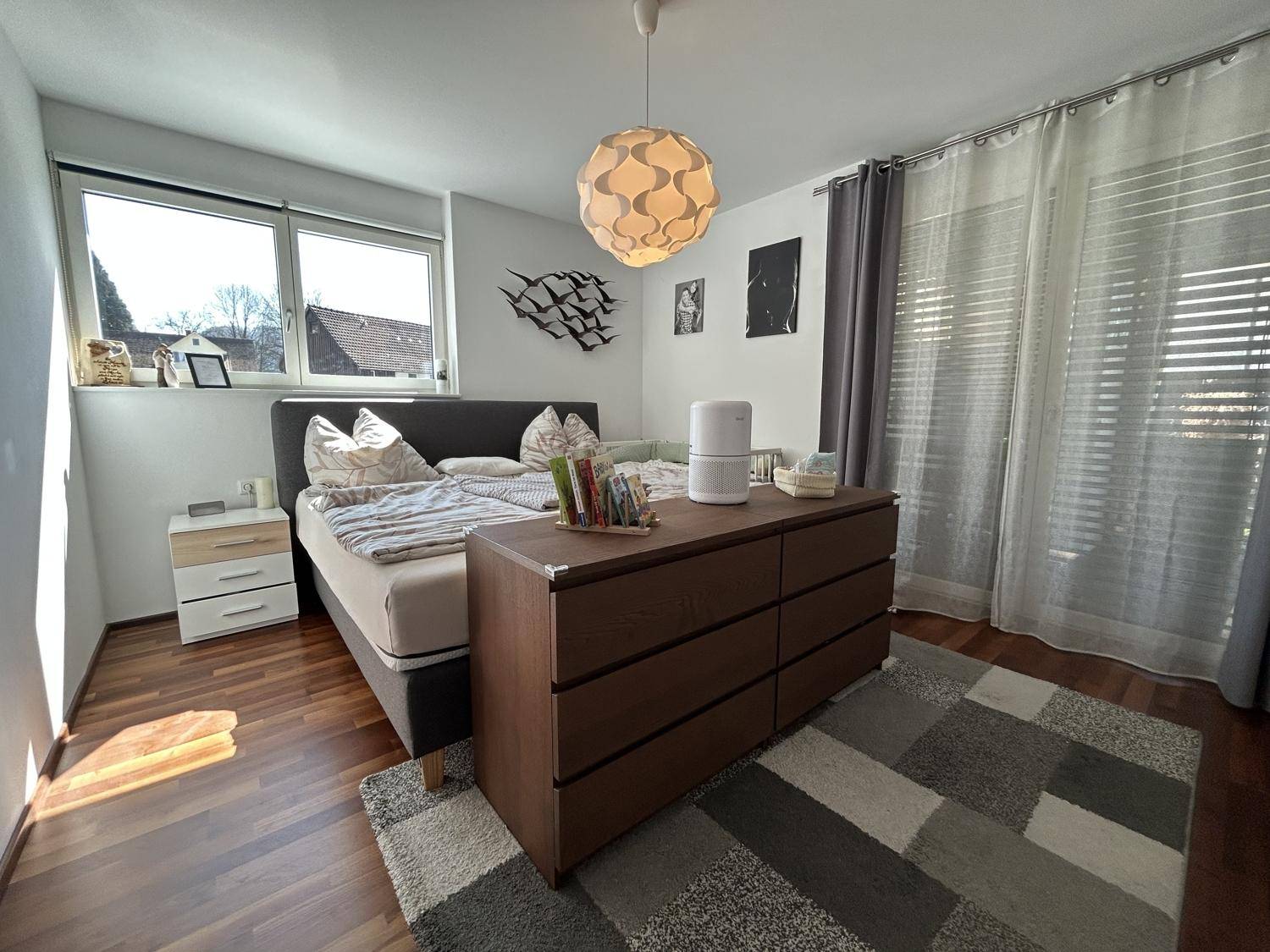 Gemütliches Schlafzimmer mit Holzboden, großem Fenster und modernem Deckenlicht.