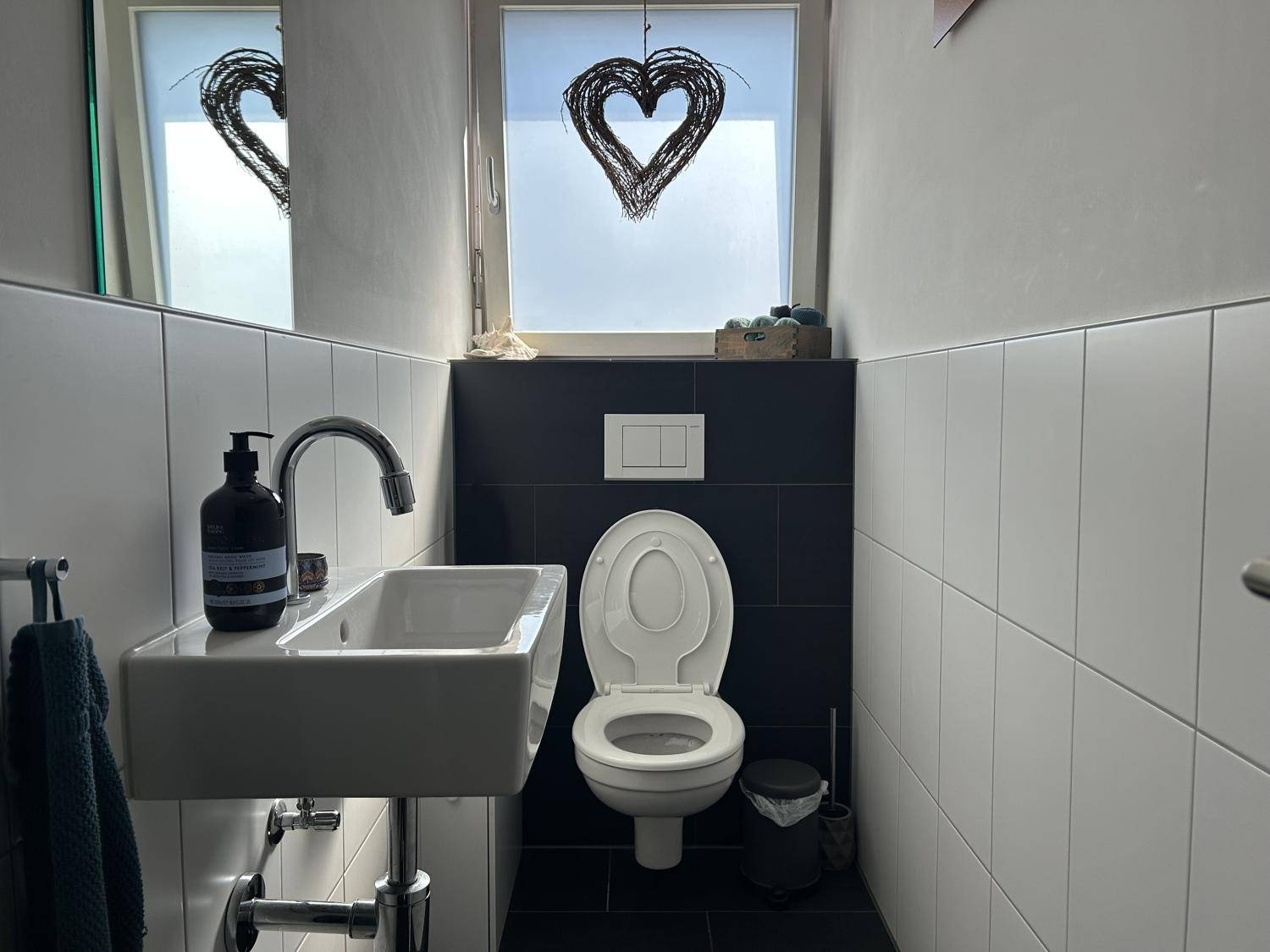 Kleines Gäste-WC mit wandhängendem WC, Handwaschbecken und Fenster.