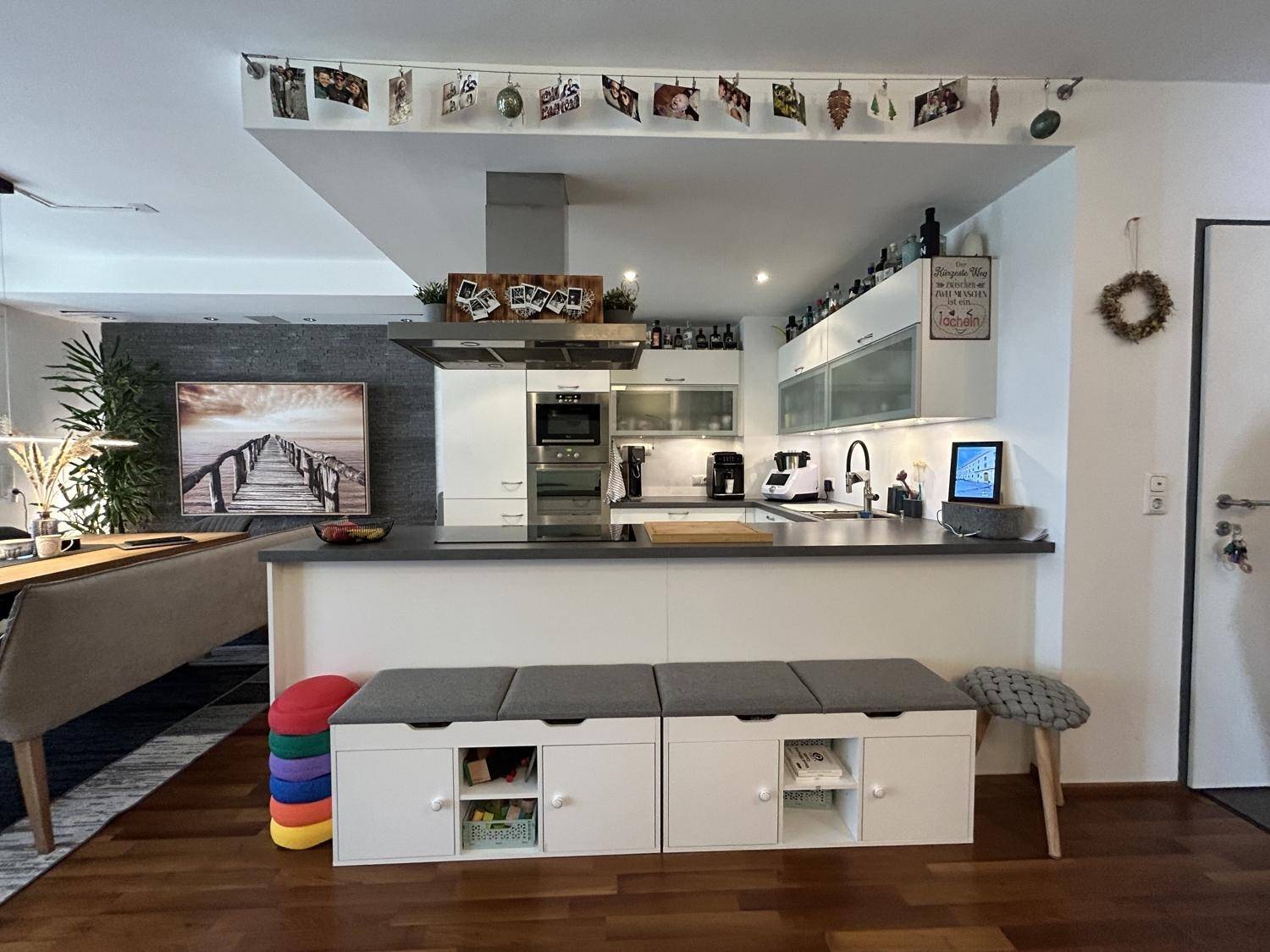 Moderne Einbauküche mit weißen Schränken, dunkler Arbeitsplatte und integriertem Essbereich.
