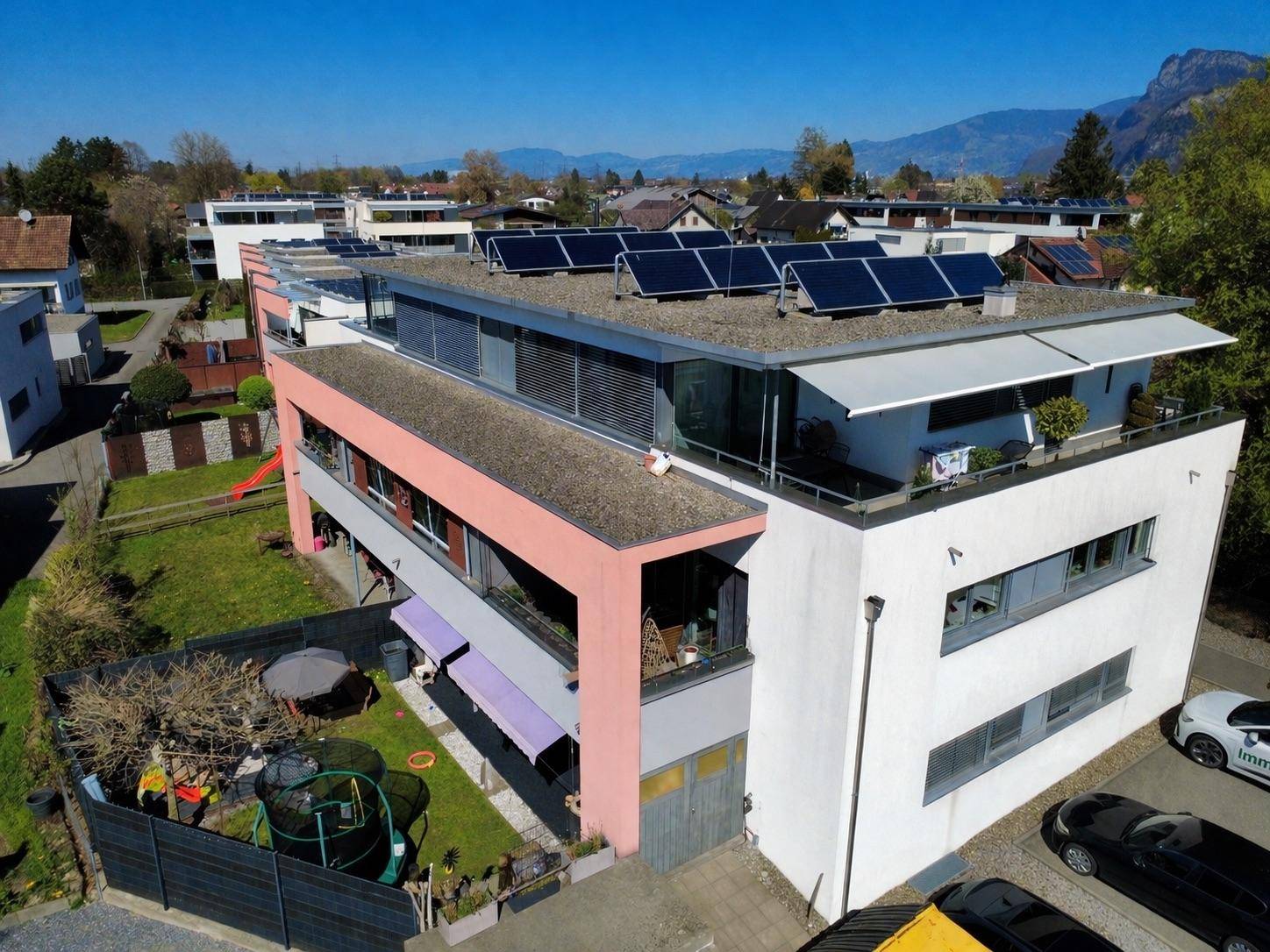 Moderne Wohnanlage mit Flachdach, Solaranlage und gepflegtem Garten unter blauem Himmel.