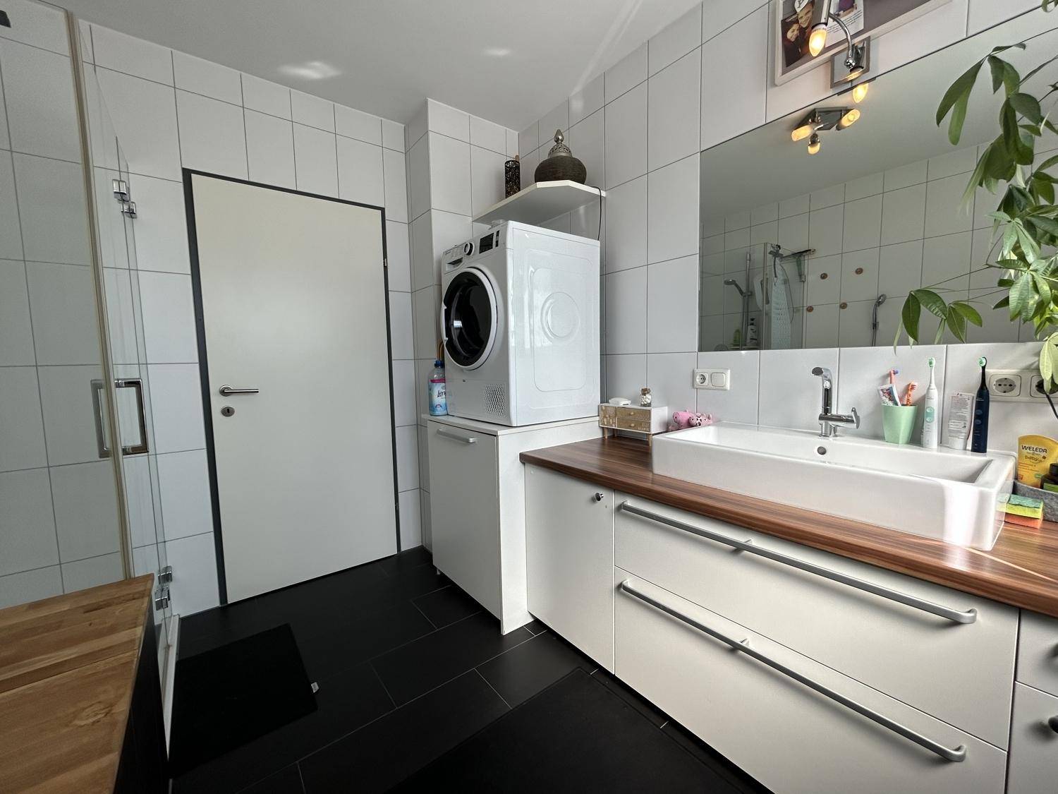 Modernes Badezimmer mit Waschmaschine, Trockner, Einzelwaschbecken und dunklen Bodenfliesen.
