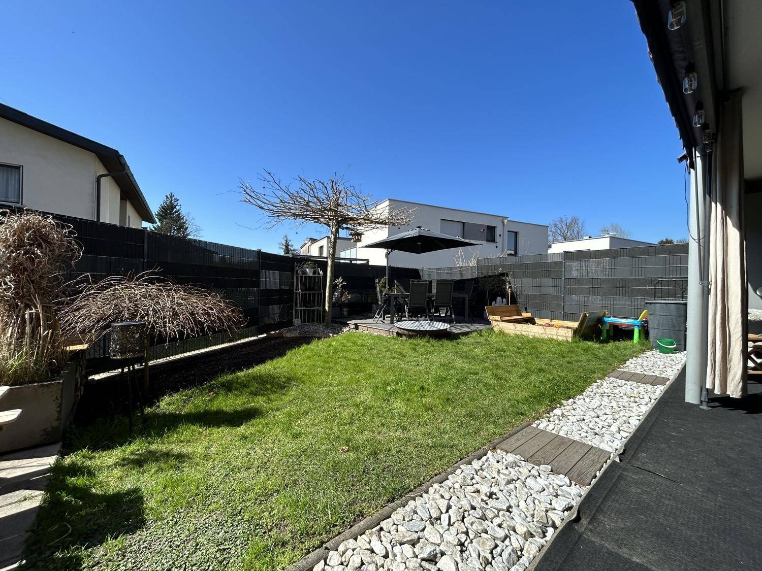 Sonniger Gartenbereich mit Rasenfläche, Kiesweg und Sitzgelegenheiten im Freien.
