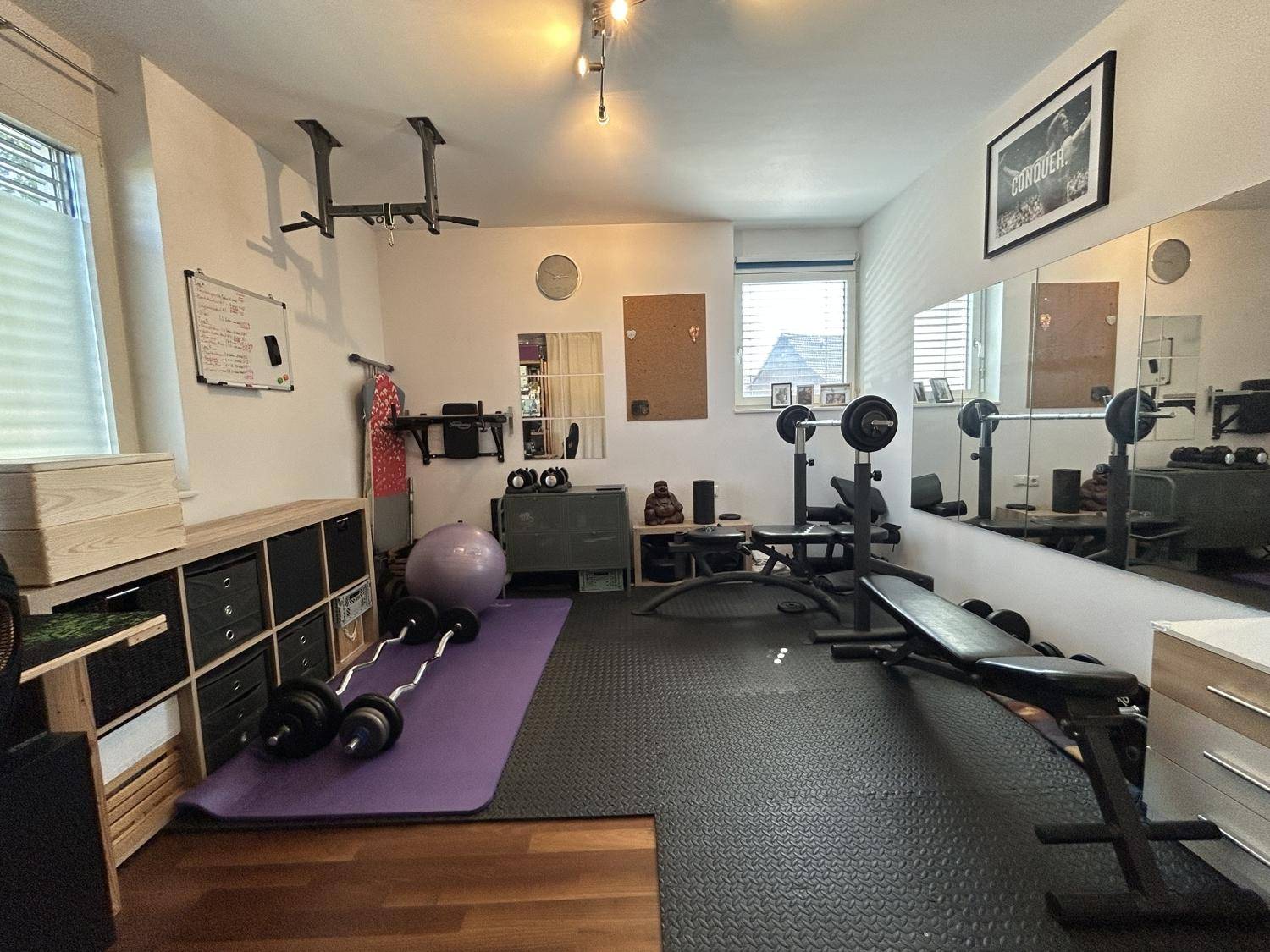 Gut ausgestatteter Fitnessraum mit Trainingsgeräten, Spiegeln und Holzboden.