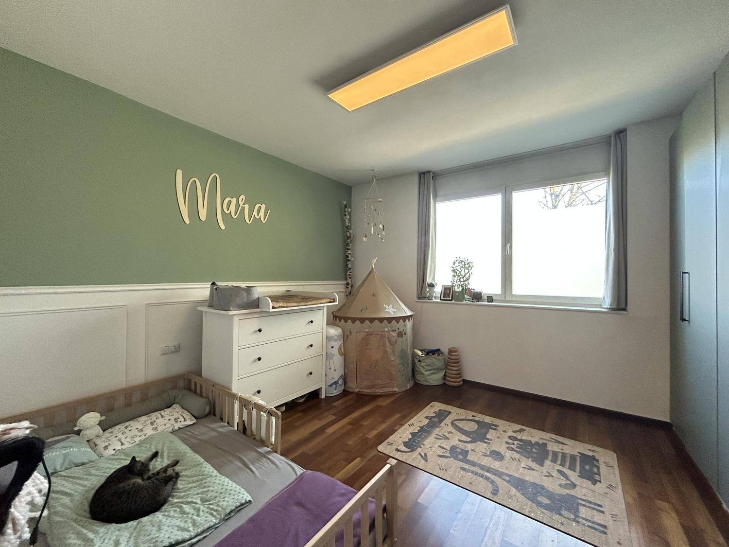 Helles Kinderzimmer mit Holzboden, Wickelkommode und einer freundlichen grünen Wand.