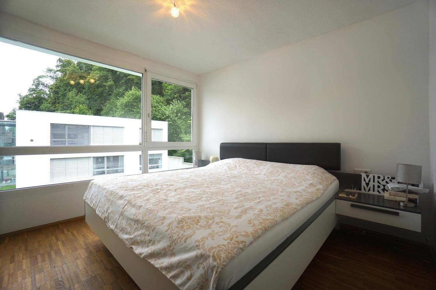 Helles Schlafzimmer mit Doppelbett, Nachttischen und großem Fenster mit Blick ins Grüne.