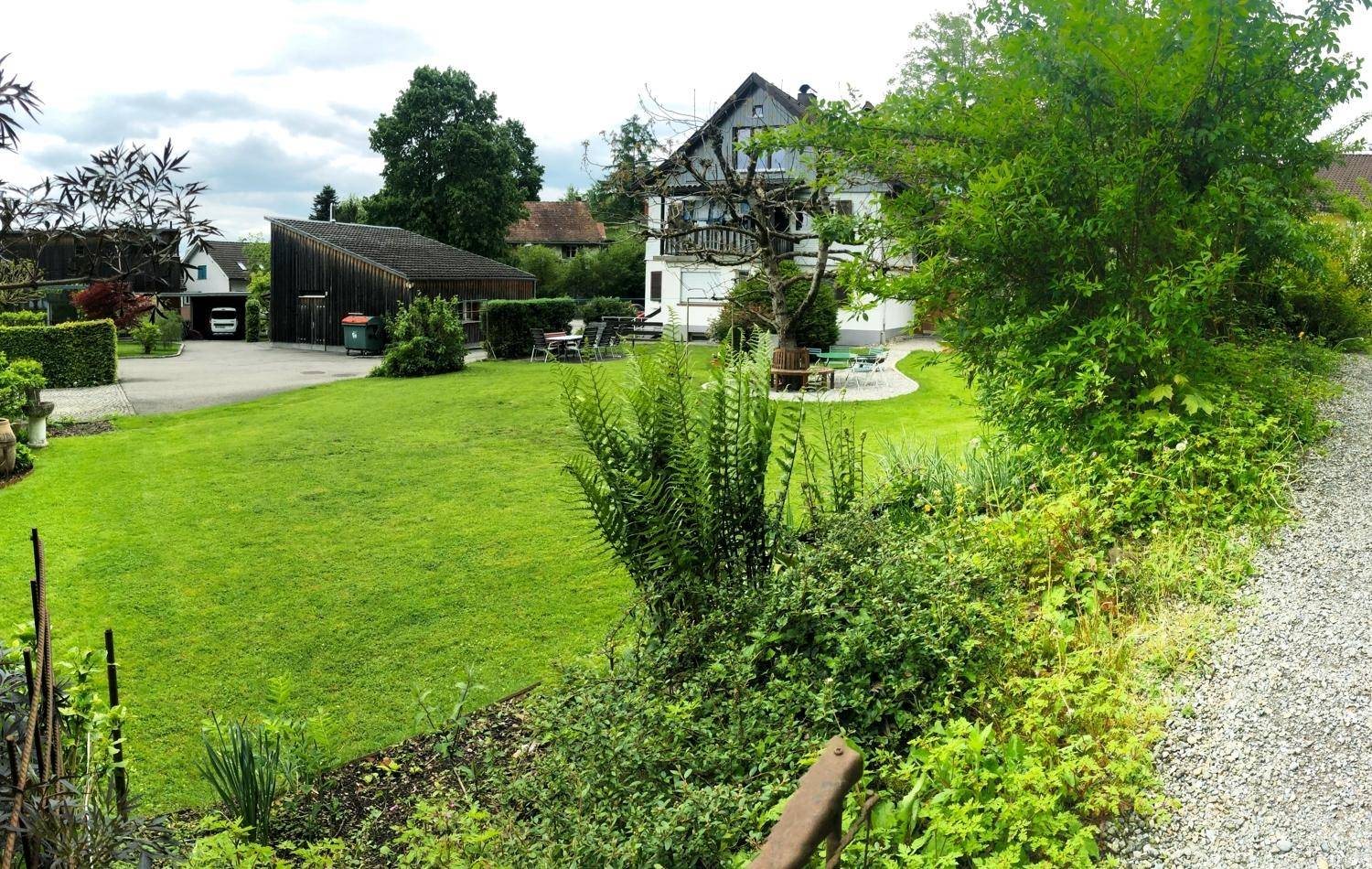 Weitläufiger Gartenbereich mit Rasen, Sträuchern und Blick auf das Haupthaus und Nebengebäude.