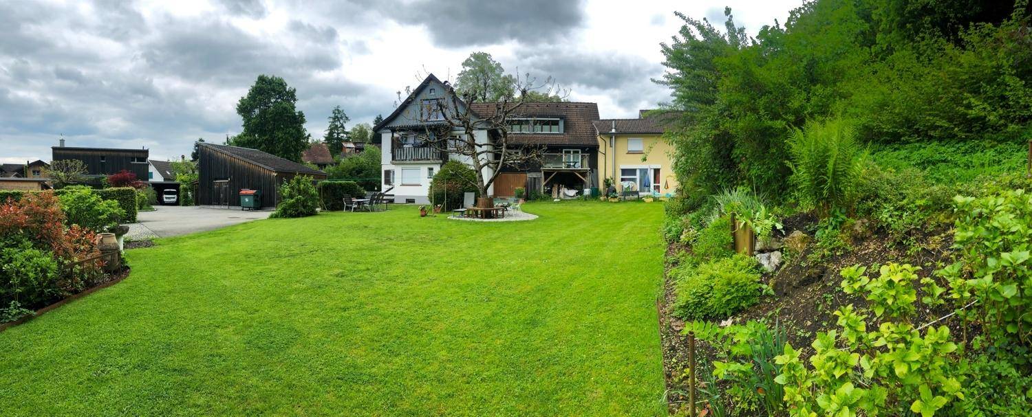 Panoramablick auf den weitläufigen Garten mit großer Rasenfläche und dem charmanten Haupthaus.