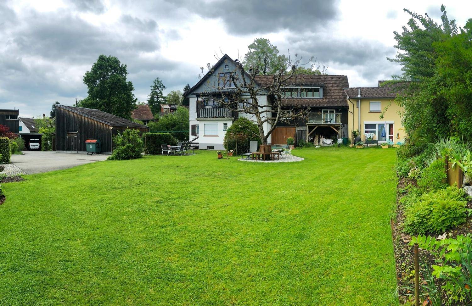 Gepflegter Garten mit großer Rasenfläche und dem Haupthaus im Hintergrund unter bewölktem Himmel.