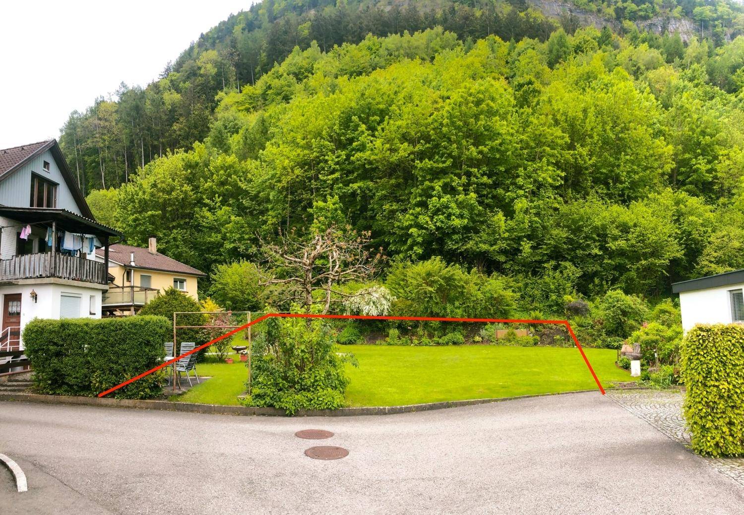 Gartenbereich mit Rasenfläche und Sträuchern, die Grundstücksgrenze ist rot markiert.