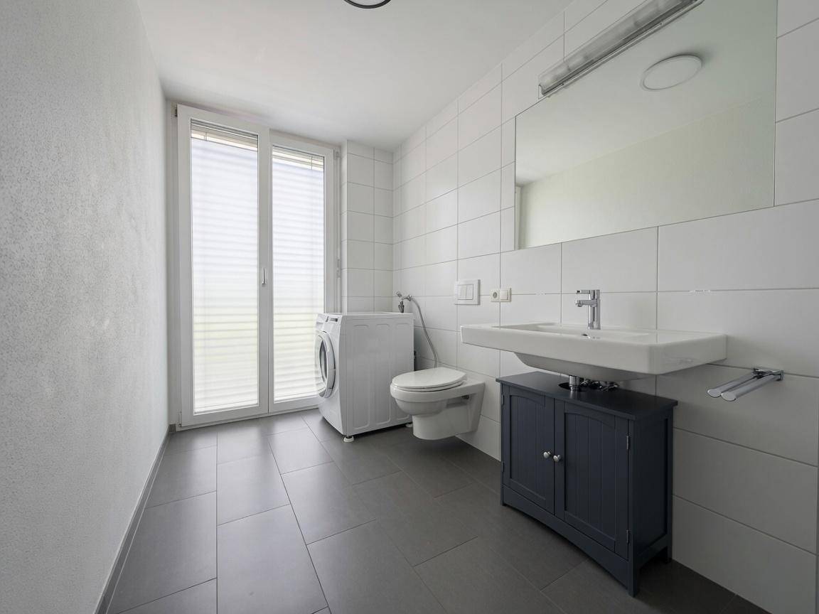 Modernes Badezimmer mit Waschbecken, Toilette, Waschmaschine und großem Fenster für Tageslicht.