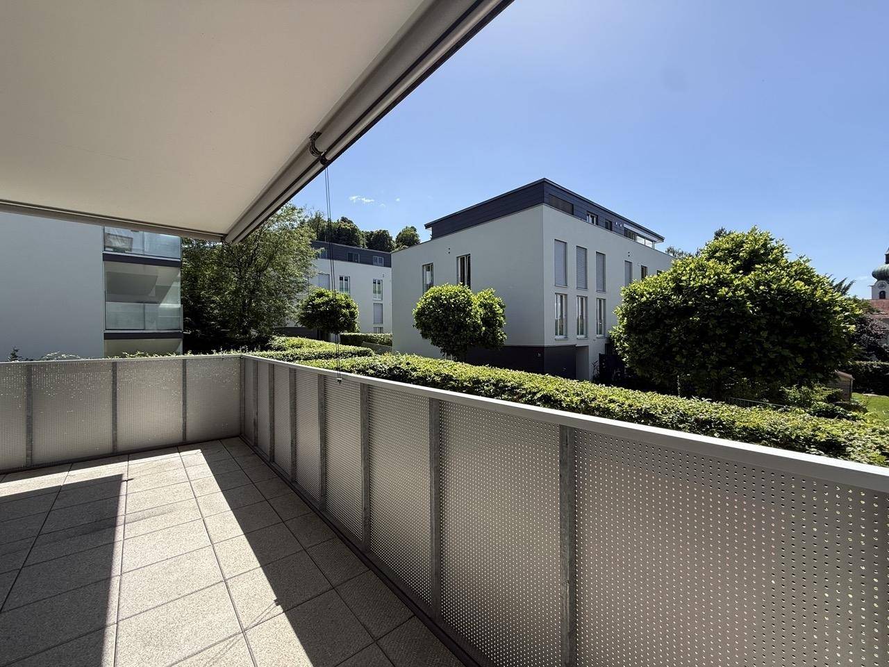 Geräumiger Balkon mit Fliesenboden und Blick auf die umliegenden modernen Gebäude und Grünflächen.