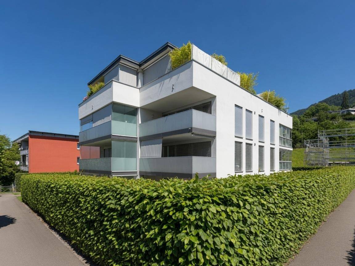 Zeitgenössisches Wohngebäude mit klaren Linien und großen Fenstern, umgeben von grünen Hecken.