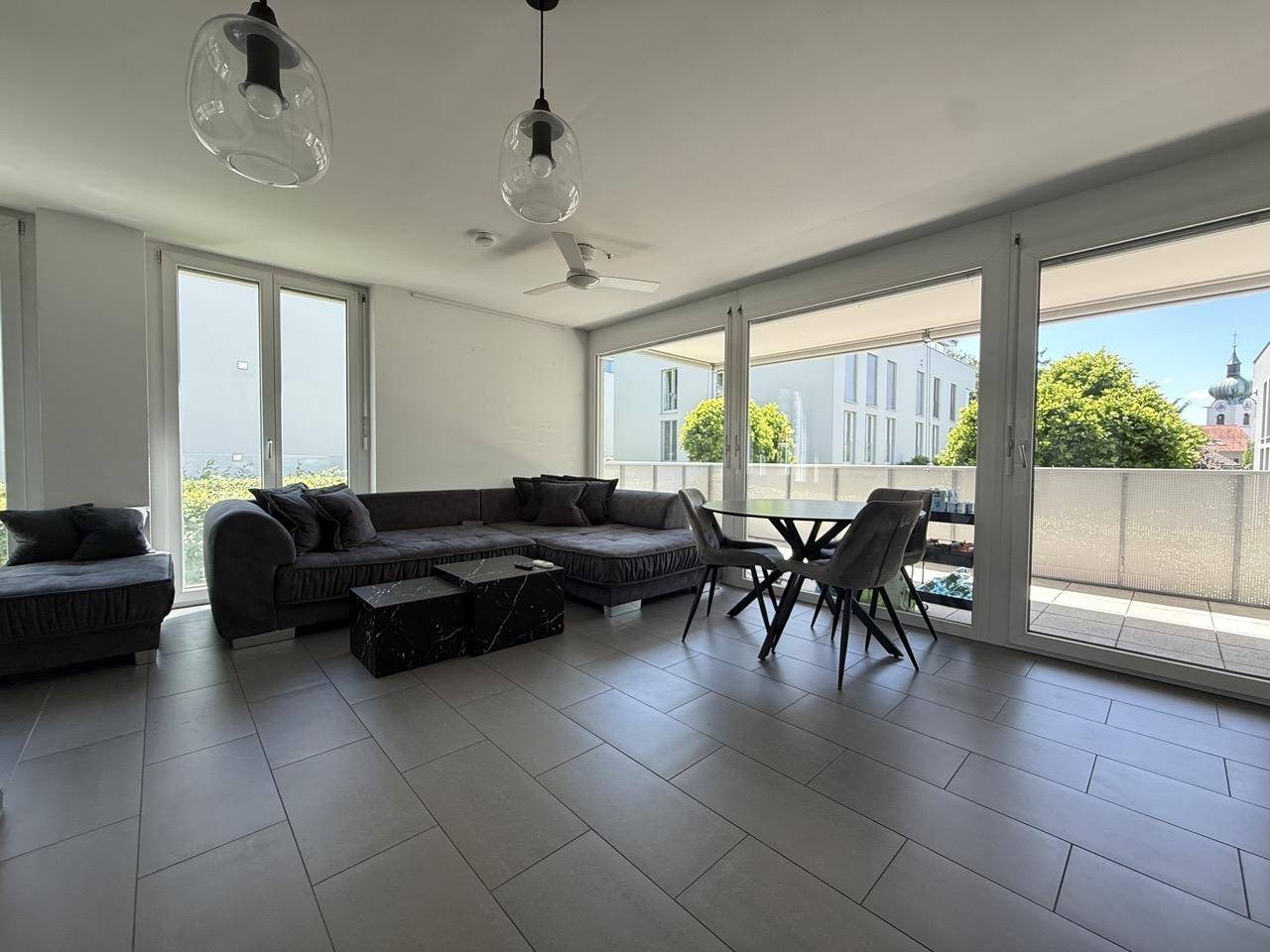 Geräumiger Wohn-Essbereich mit großem Sofa, Esstisch und Zugang zu einem sonnigen Balkon.