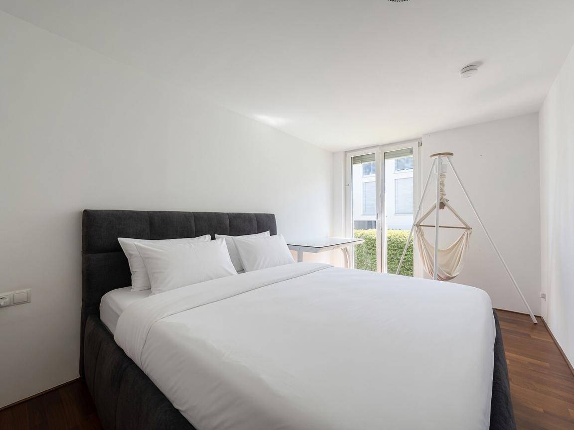Helles Schlafzimmer mit modernem Bett, Holzboden und Zugang zu einem kleinen Außenbereich.