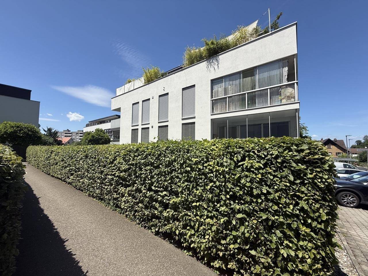 Moderne Wohnanlage mit gepflegter Hecke und Parkplätzen im Freien unter blauem Himmel.