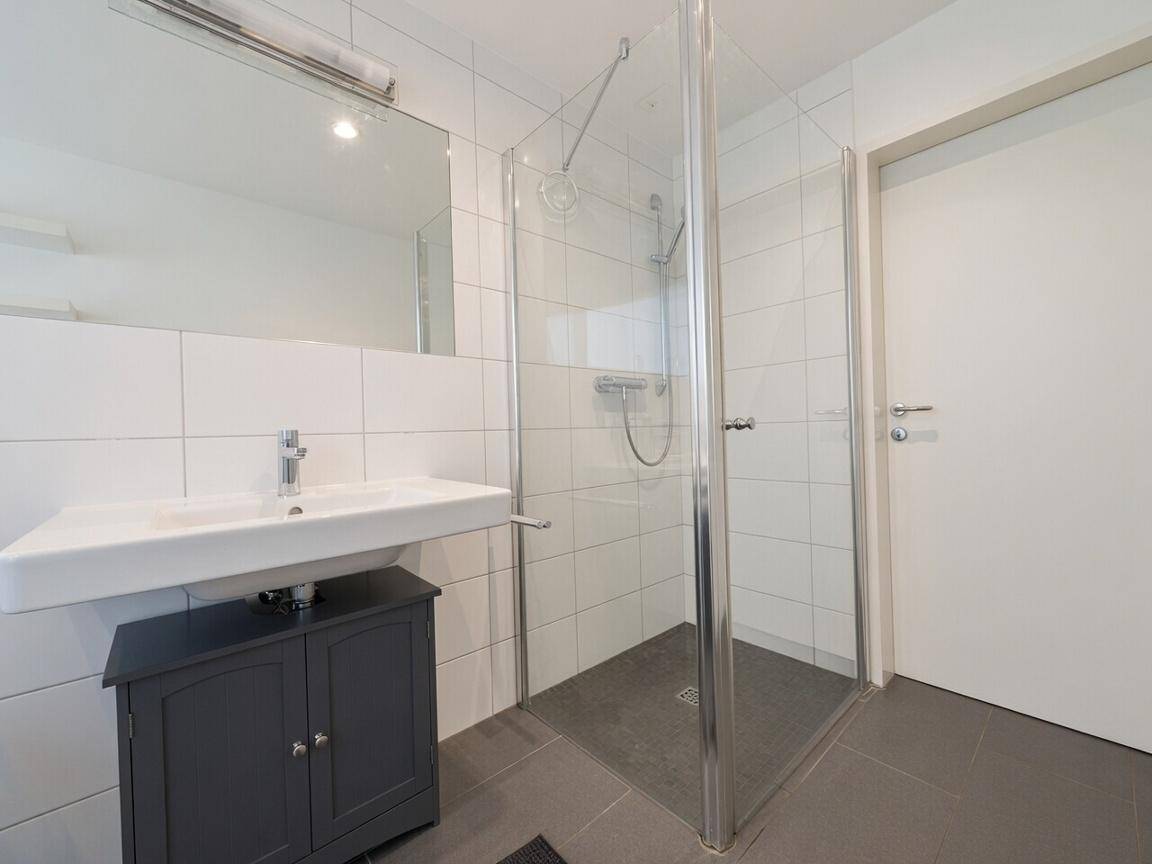 Helles Badezimmer mit moderner Duschkabine, Waschbecken und großem Spiegel.