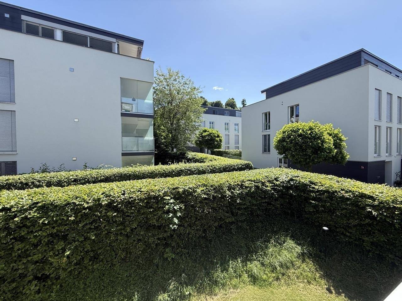 Ansicht einer modernen Wohnsiedlung mit mehreren Gebäuden und gepflegten Hecken unter blauem Himmel.