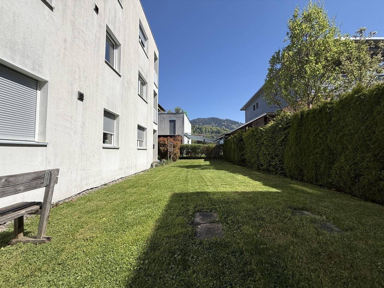 Sonniger Gartenbereich mit Rasenfläche und einer rustikalen Holzbank am Rand, ideal zum Entspannen.