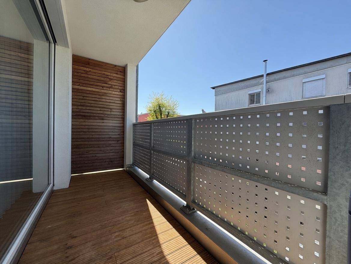Geräumiger Balkon mit Holzboden und moderner Holzverkleidung an der Wand, sonnig und einladend.