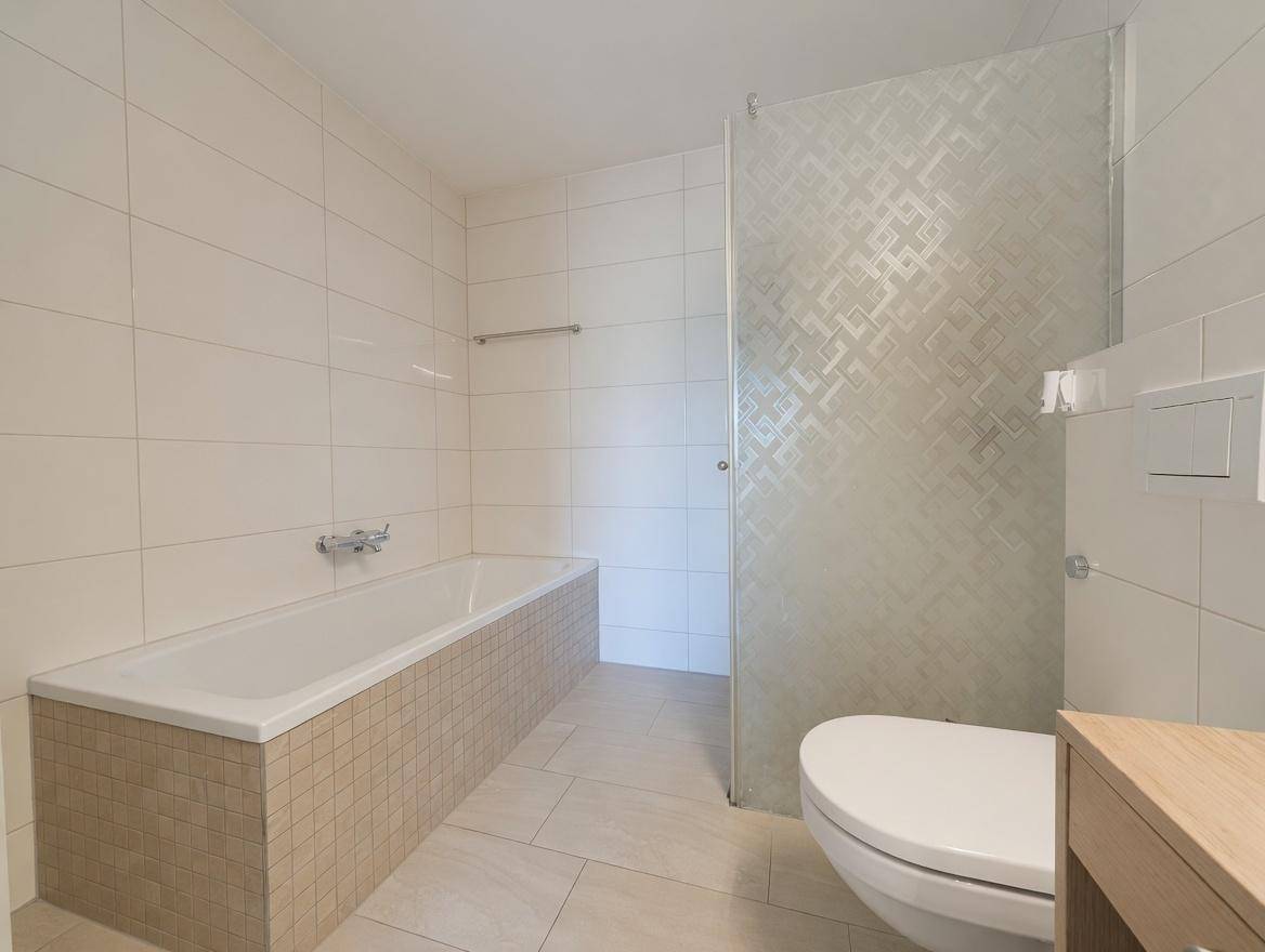 Modernes Badezimmer mit Badewanne, Dusche und hellen Fliesen an Wänden und Boden, sehr gepflegt.