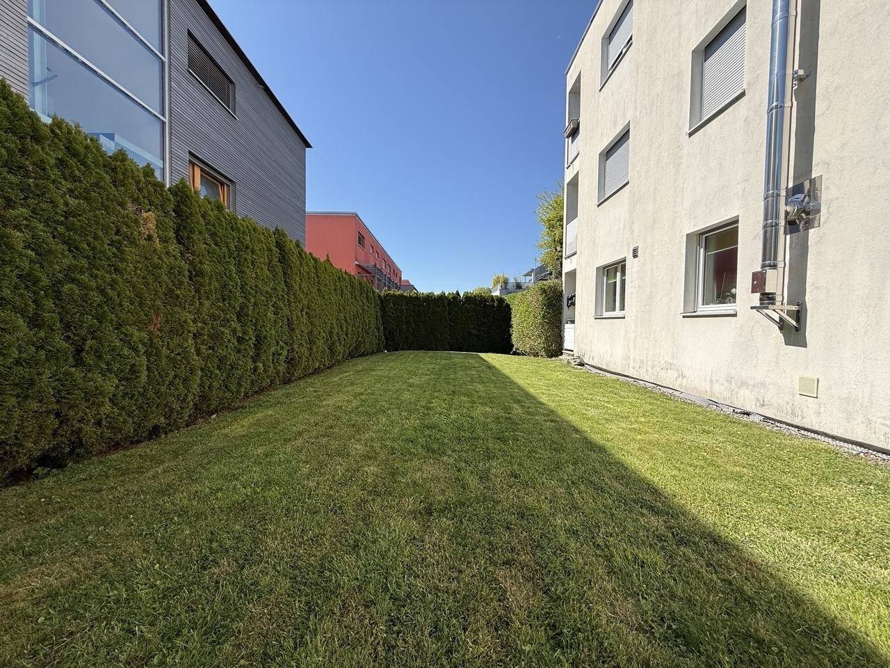 Grüne Rasenfläche zwischen den Gebäuden, begrenzt durch eine hohe Hecke, bietet viel Privatsphäre.