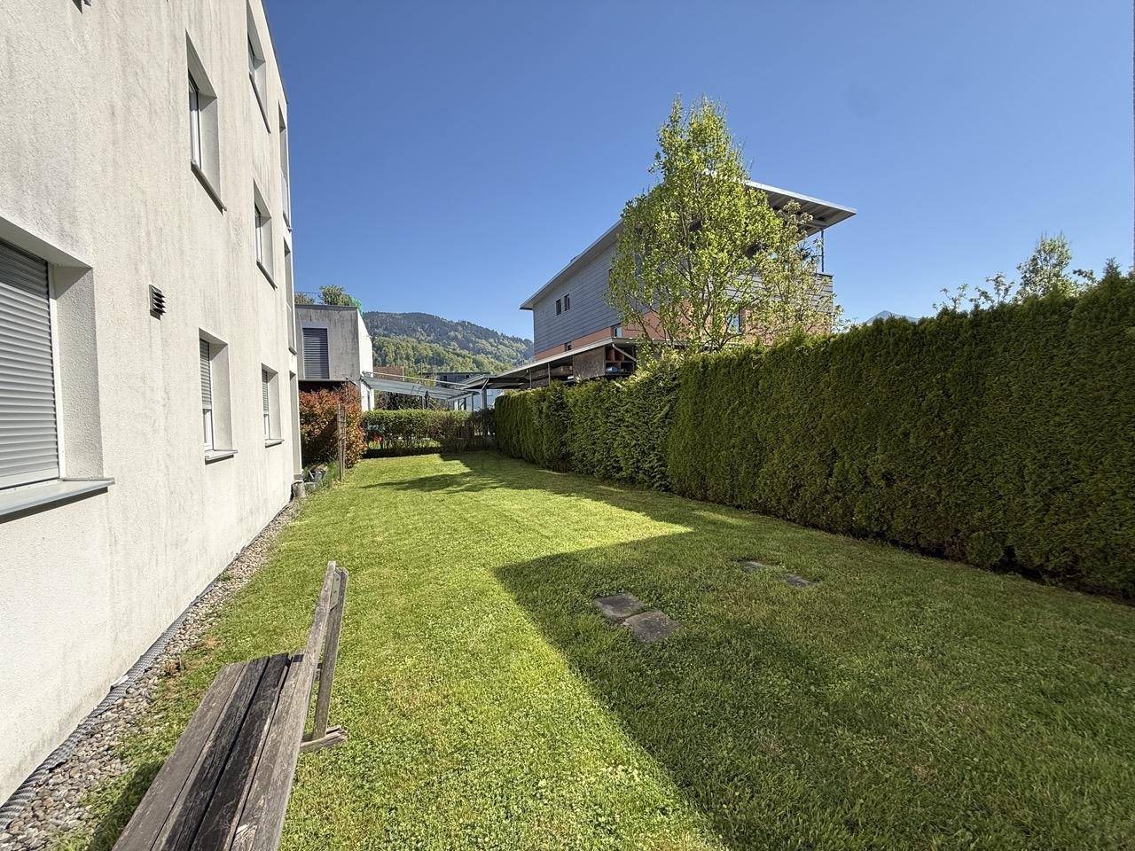 Gepflegter Rasenbereich zwischen den Gebäuden, umgeben von einer hohen, grünen Hecke.
