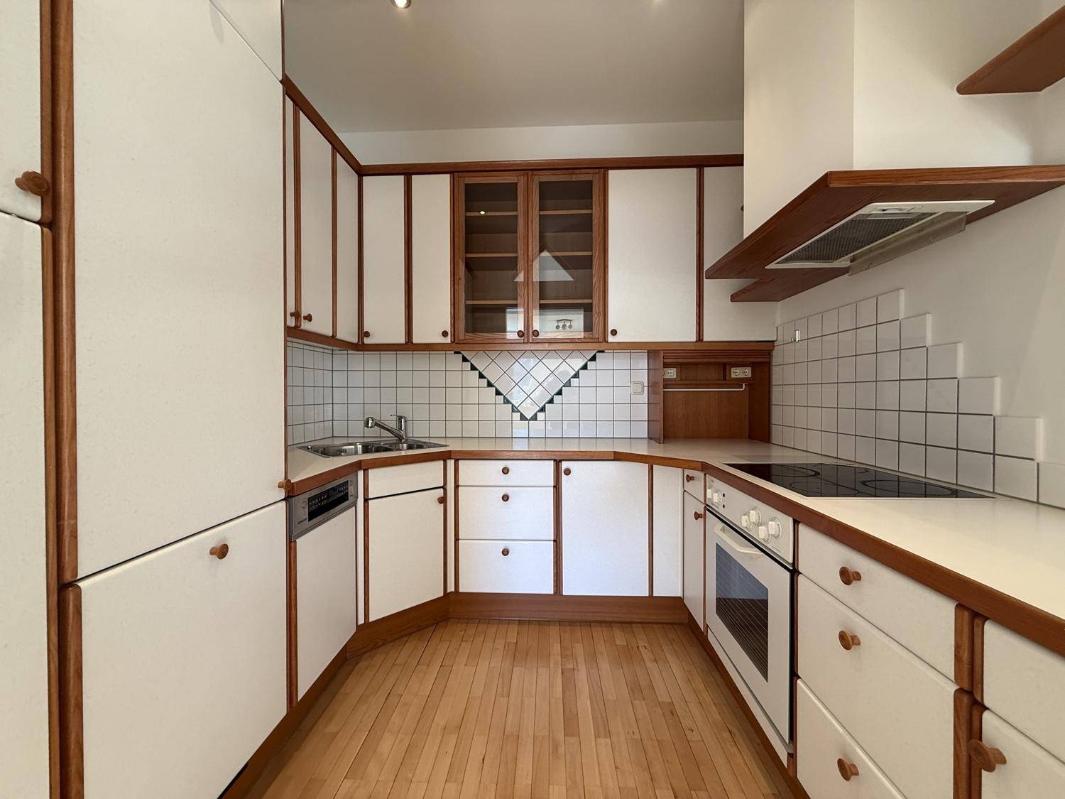 Funktionale Einbauküche mit weißen Fronten, Holzdetails und Fliesenboden.