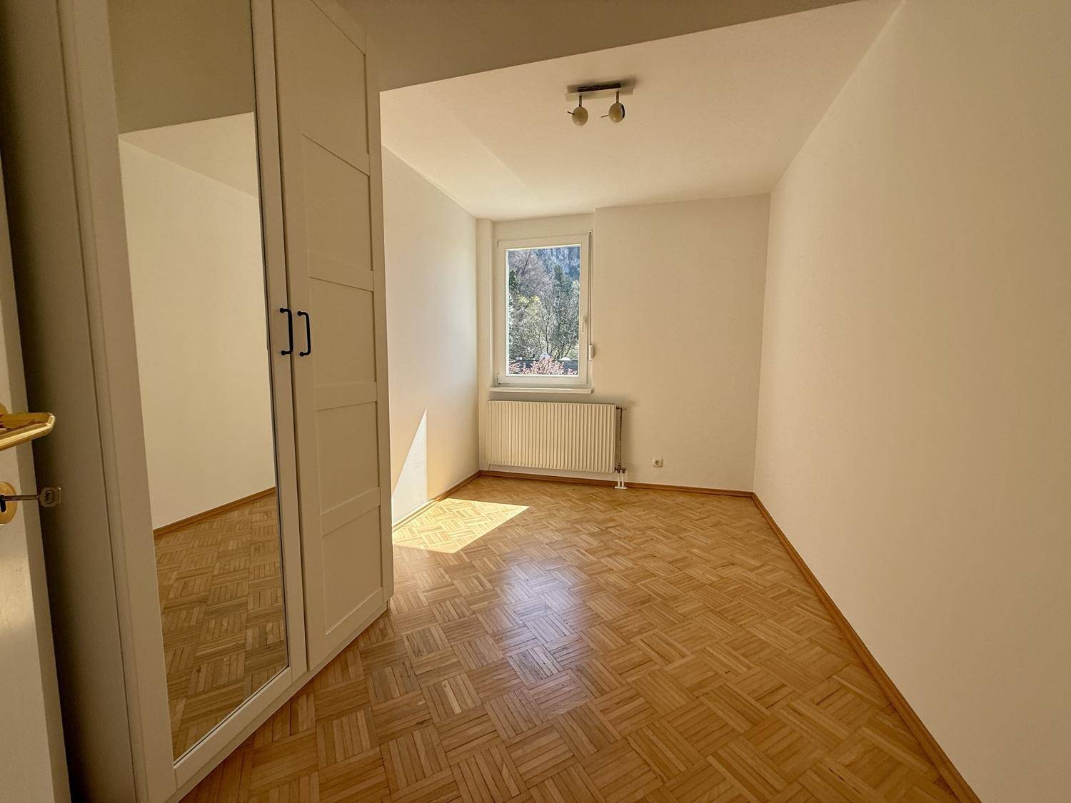 Helles Schlafzimmer mit Parkettboden und Fenster mit Blick ins Grüne.