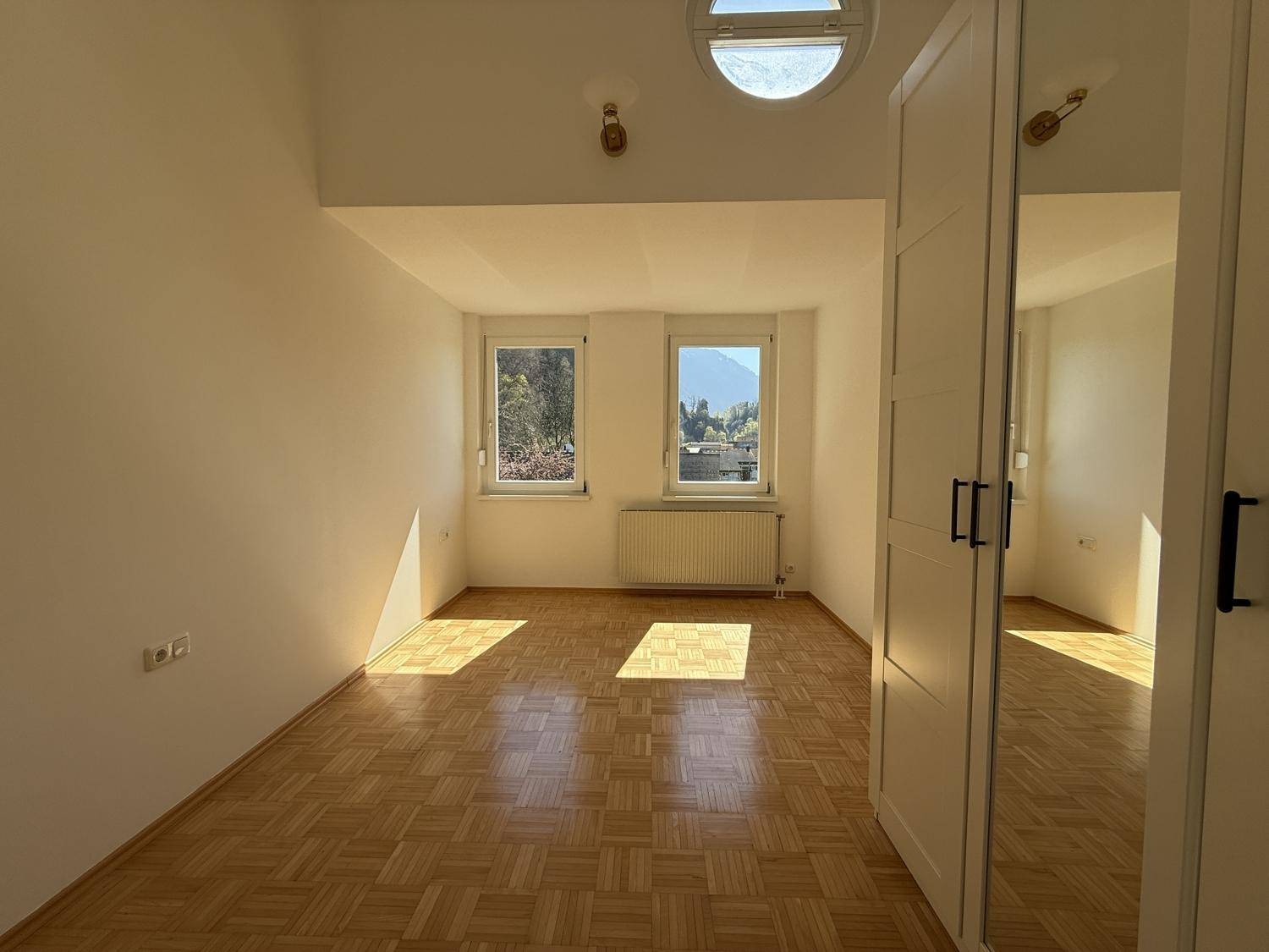 Lichtdurchflutetes Schlafzimmer mit Parkettboden und zwei Fenstern.