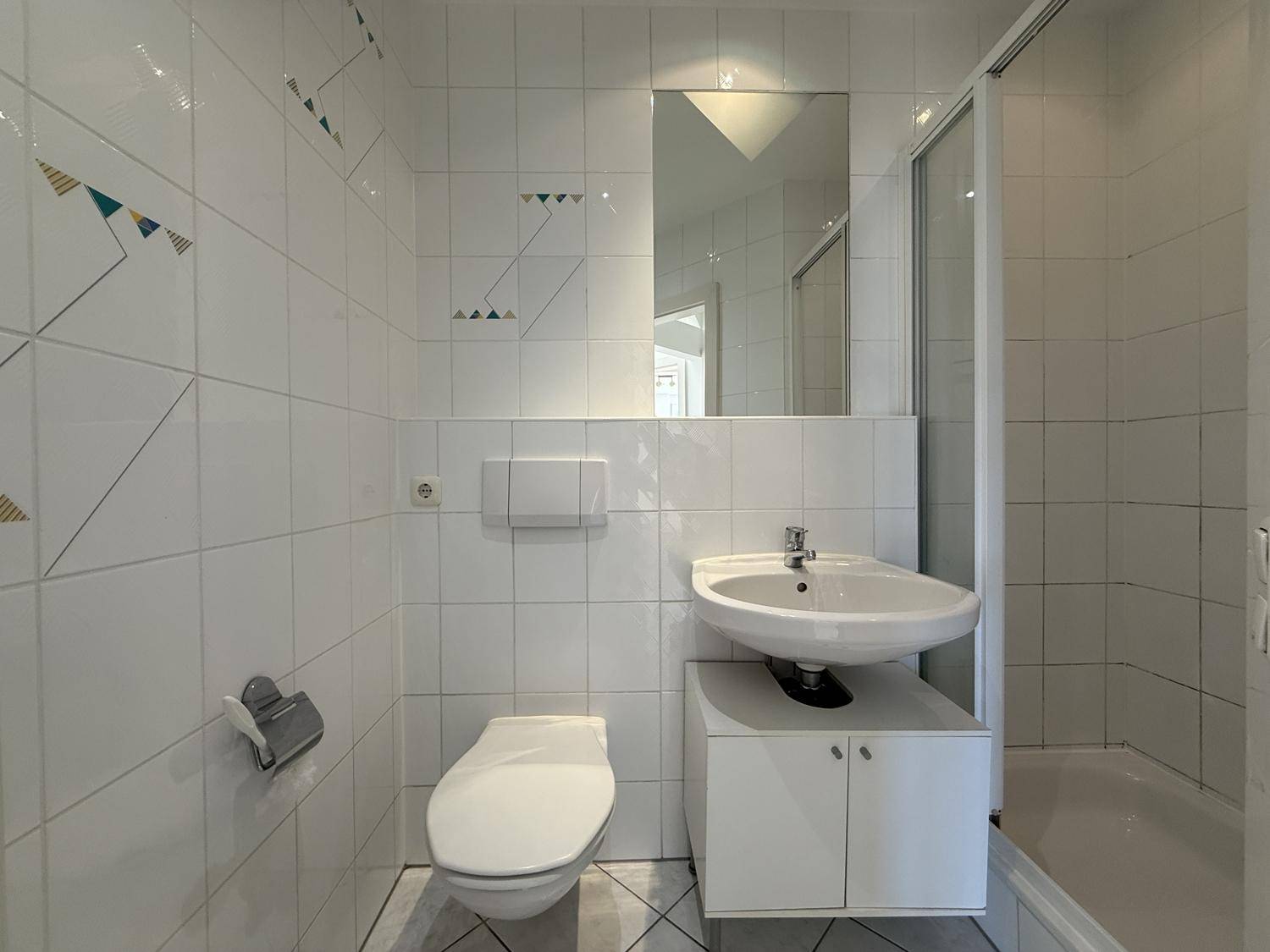 Gefliestes Badezimmer mit Dusche, WC und Waschbecken mit Unterschrank.