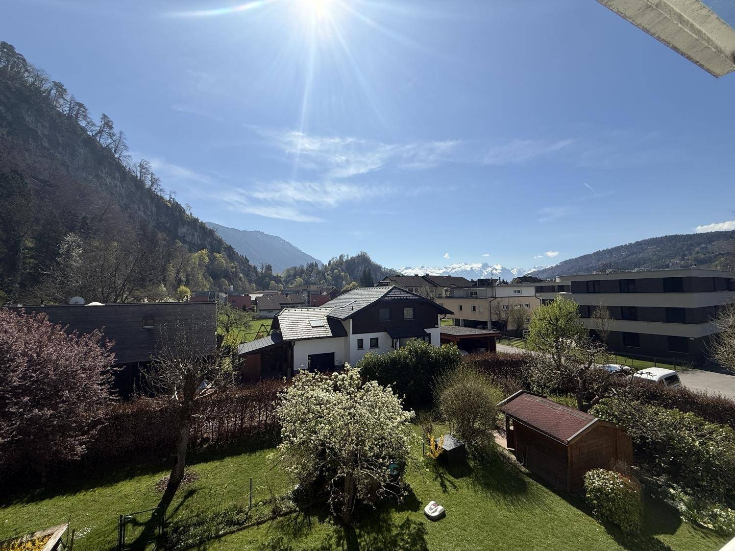 Panoramablick auf die umliegende Berglandschaft und grüne Gärten an einem sonnigen Tag.