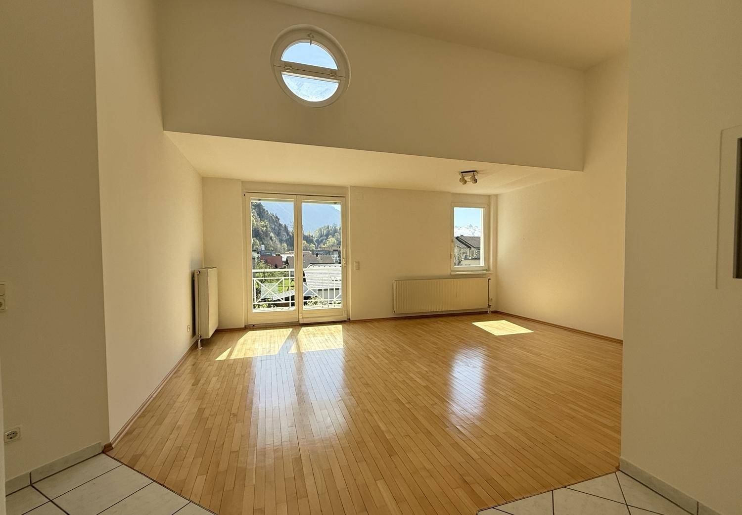 Helles Wohnzimmer mit Parkettboden, hohen Decken und Zugang zum Balkon.