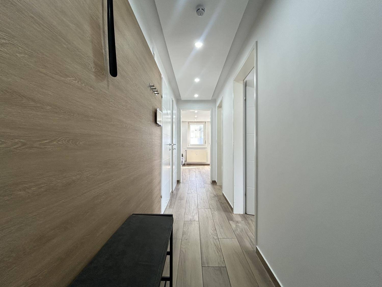 Heller Flur mit Holzoptikboden, moderner Wandverkleidung und integrierter Deckenbeleuchtung.