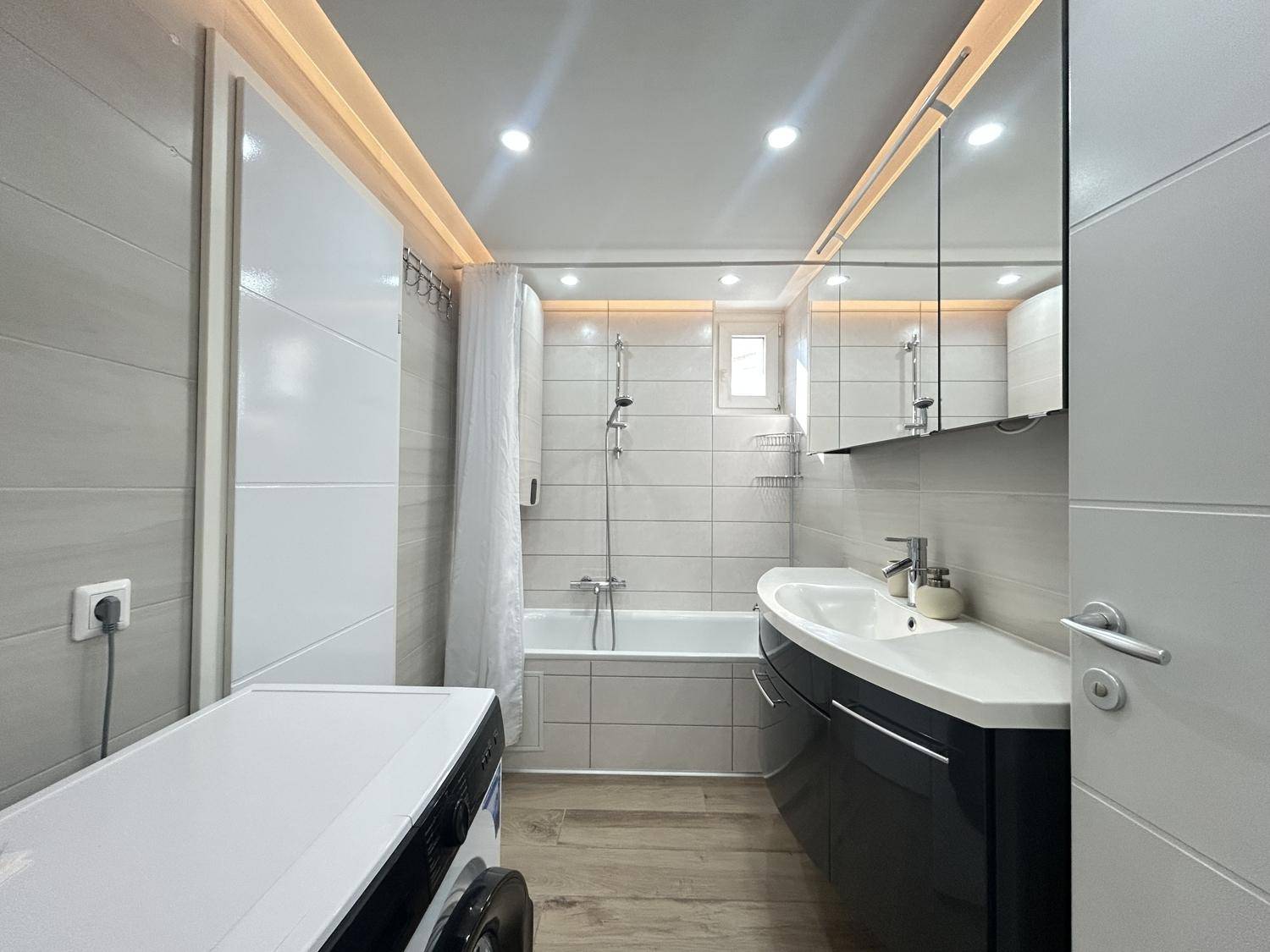 Modernes Badezimmer mit Badewanne, Dusche, Einzelwaschbecken und integrierter Waschmaschine.