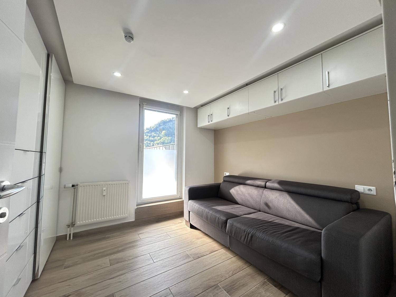 Gemütliches Wohnzimmer mit Sofa, Holzoptikboden und praktischen Einbauschränken über dem Sitzbereich.