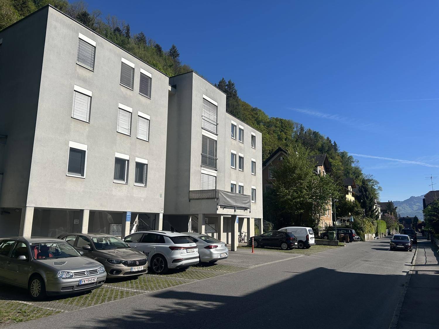 Modernes Mehrfamilienhaus mit Parkplätzen vor dem Gebäude und grüner Umgebung.