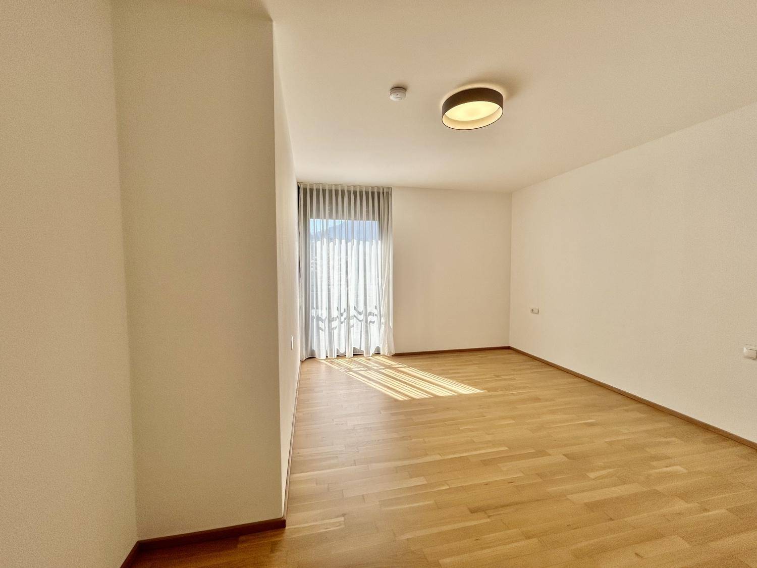 Helles Zimmer mit Parkettboden und großem Fenster, das viel Tageslicht hereinlässt.