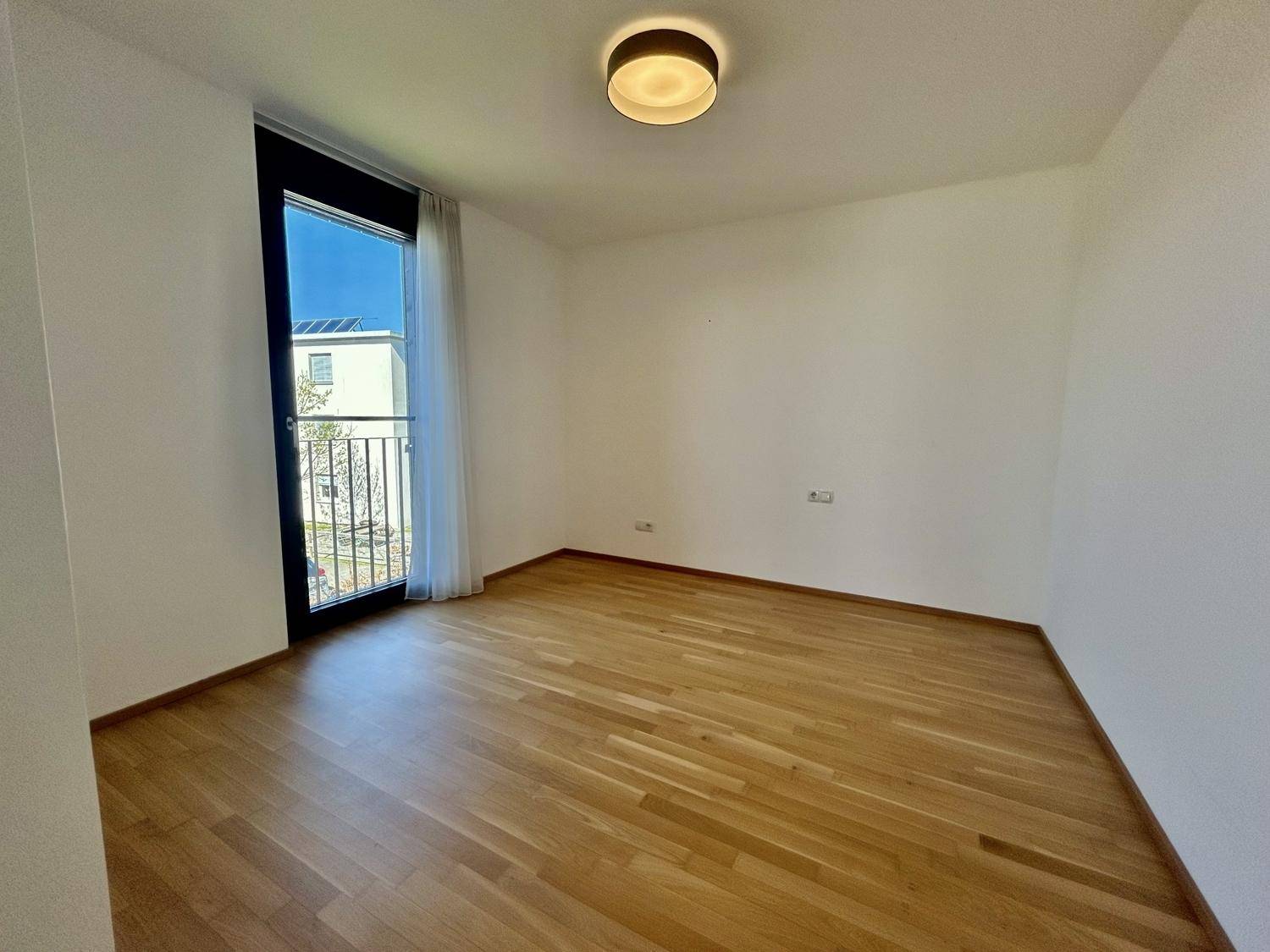 Geräumiges Zimmer mit Holzboden und Zugang zu einem französischen Balkon, sehr hell.