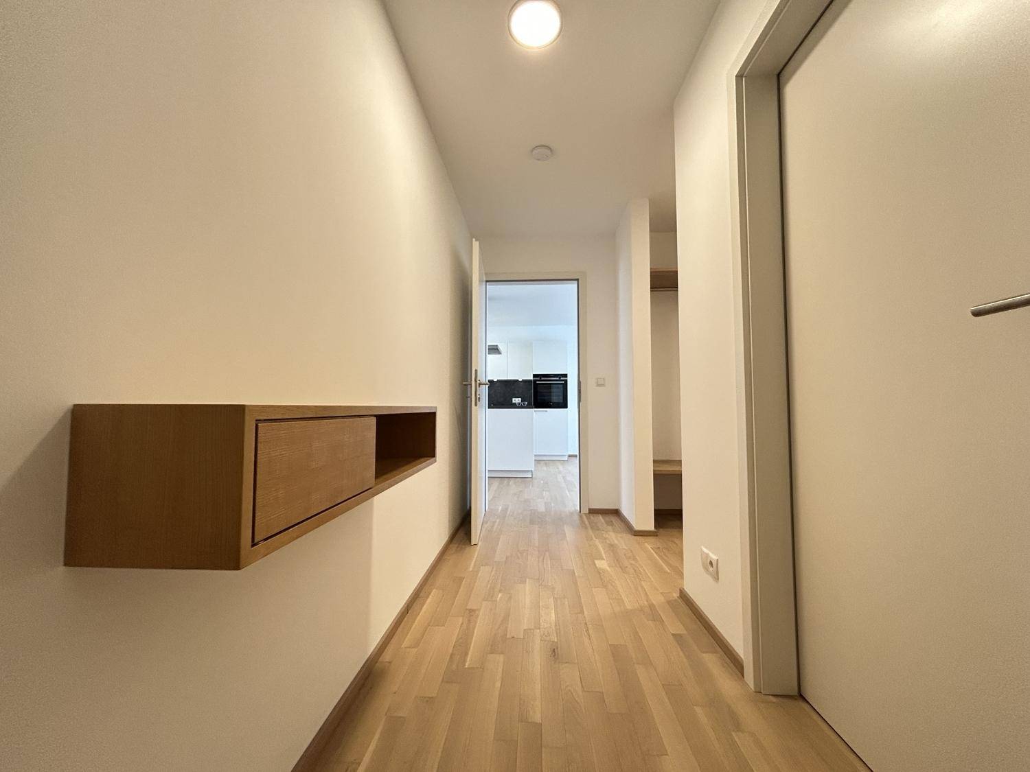 Heller Flur mit modernem Holzregal und Eichenparkettboden, der zur Küche führt.