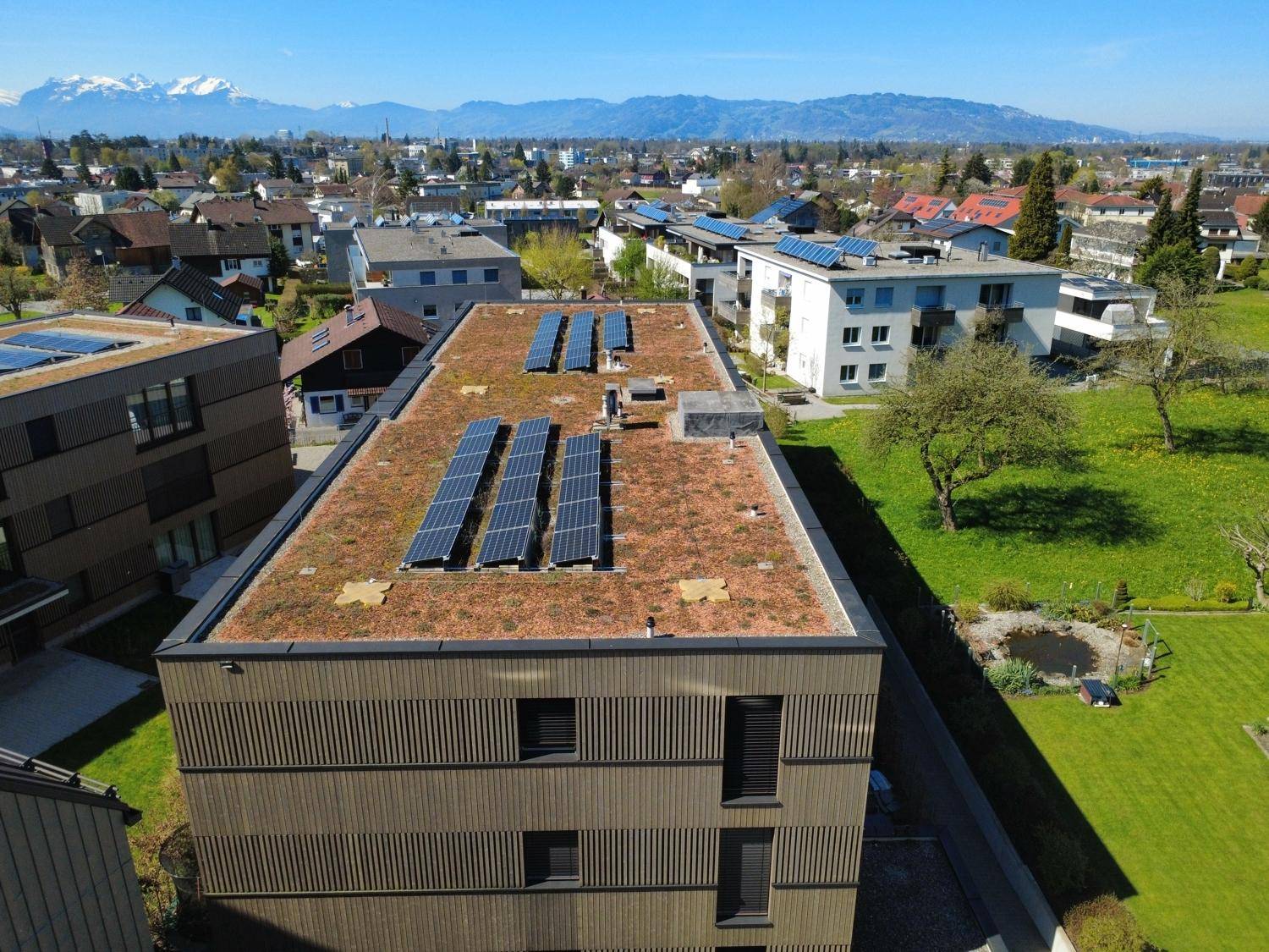 Luftaufnahme eines modernen Gebäudes mit Gründach und Photovoltaikanlage, umgeben von Natur.