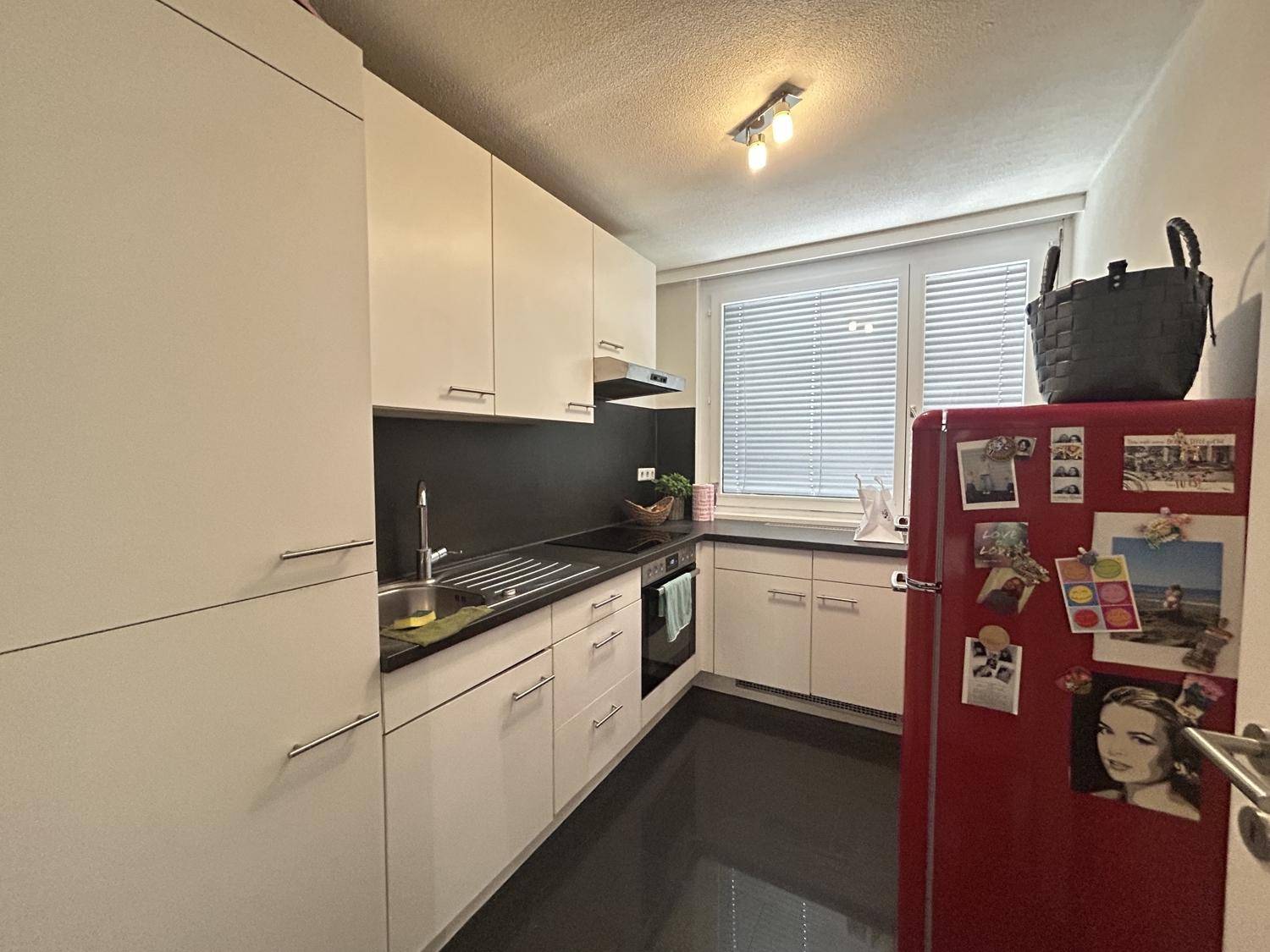 Funktionale Küche mit weißen Schränken, dunkler Arbeitsplatte und einem roten Kühlschrank.