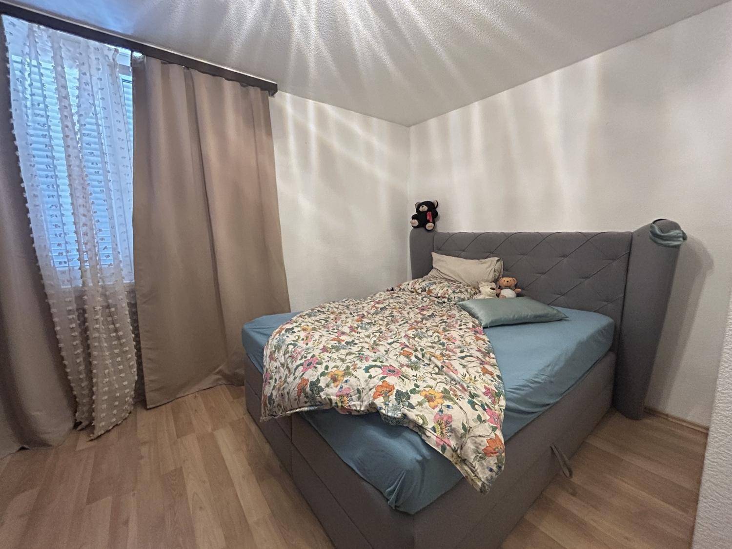 Schlafzimmer mit Laminatboden und einem bequemen Bett neben dem Fenster.