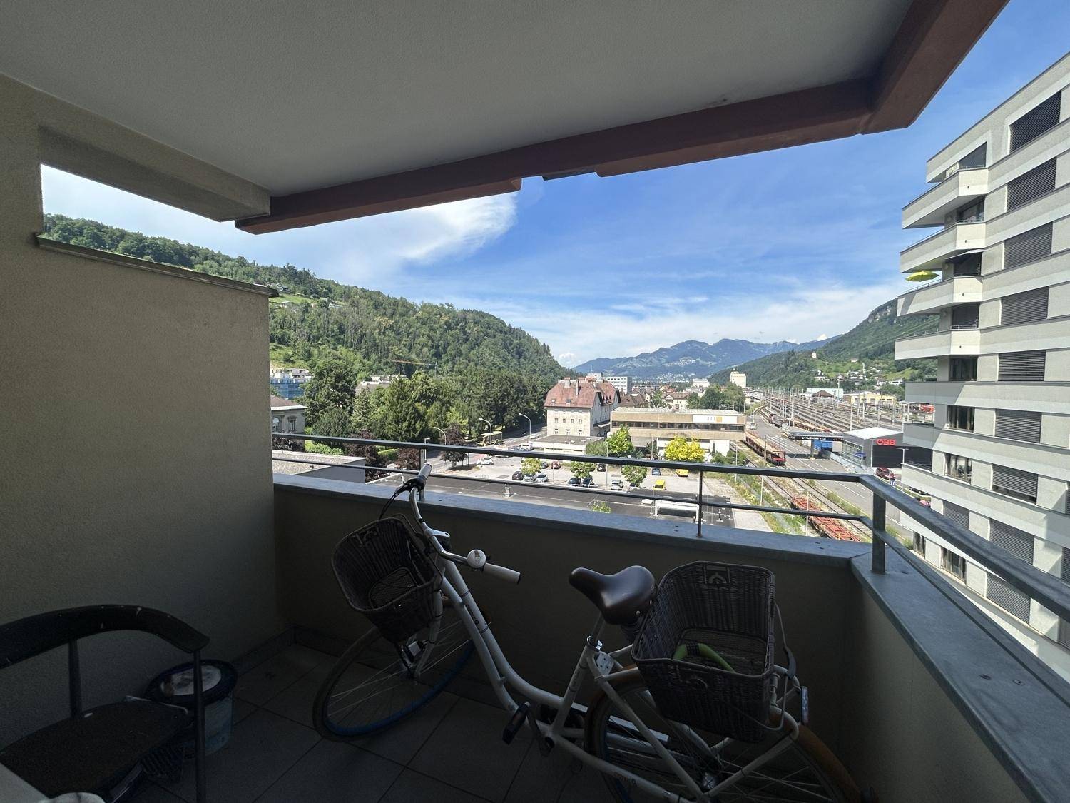 Balkon mit Fahrrad und weitem Blick über die Stadt und die umliegenden Berge.