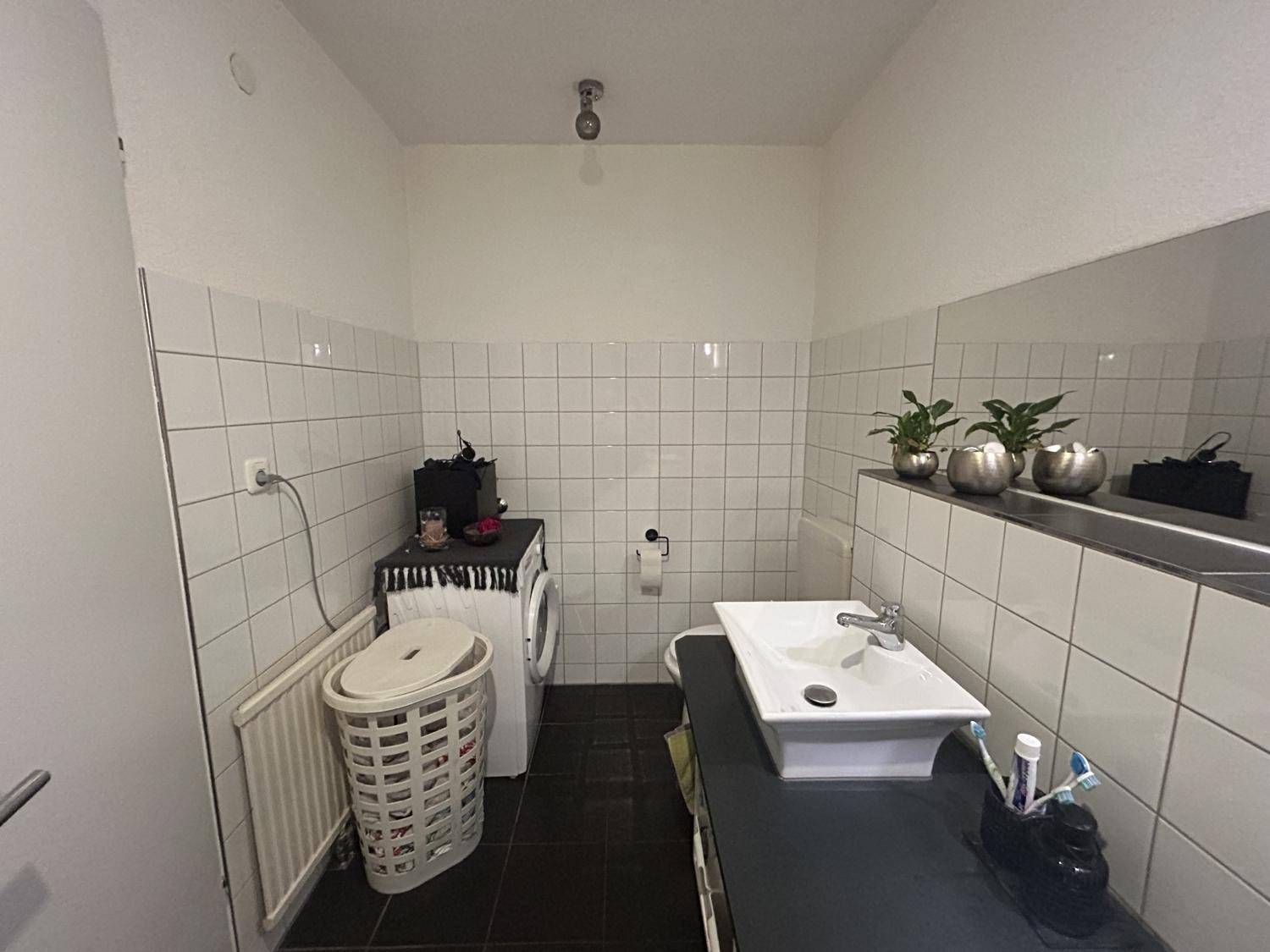 Separates WC mit Waschbecken, Toilette und Platz für eine Waschmaschine.