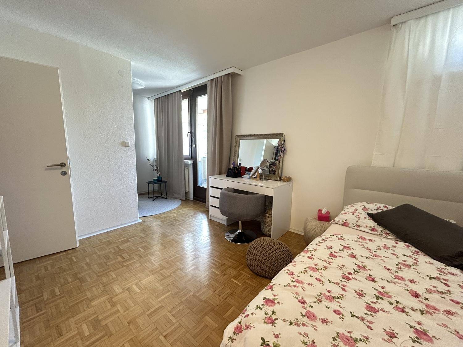 Helles Schlafzimmer mit Parkettboden und Zugang zu einem weiteren Raum.