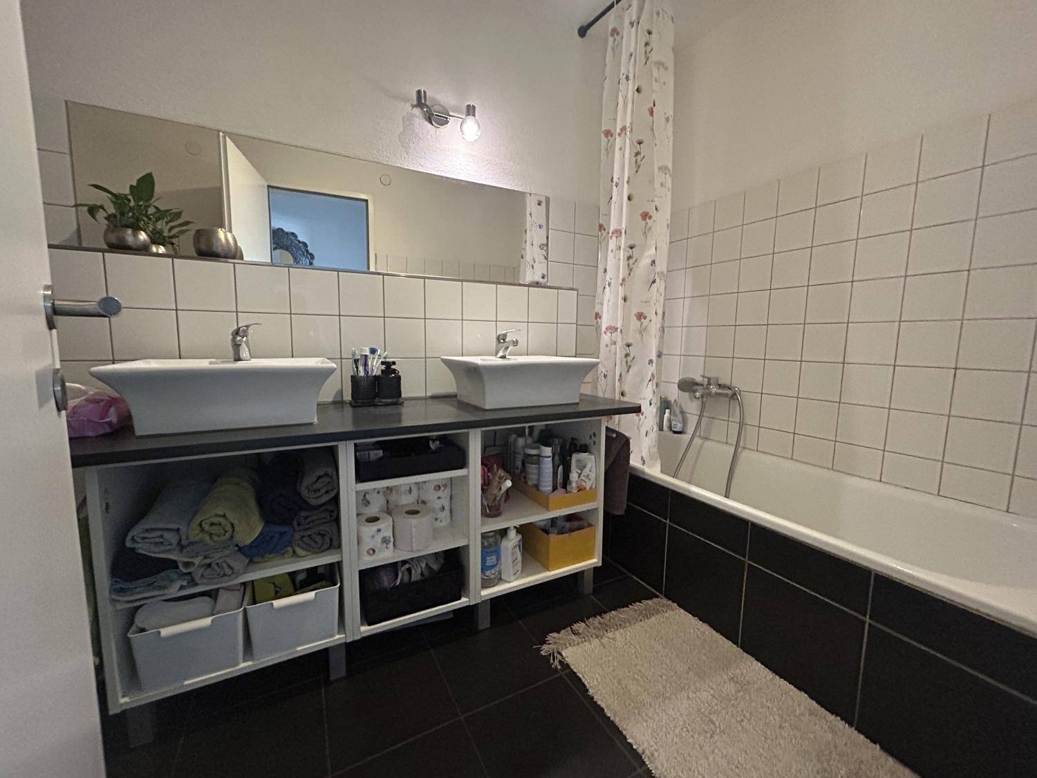 Badezimmer mit Doppelwaschbecken, Badewanne und weißen sowie schwarzen Fliesen.