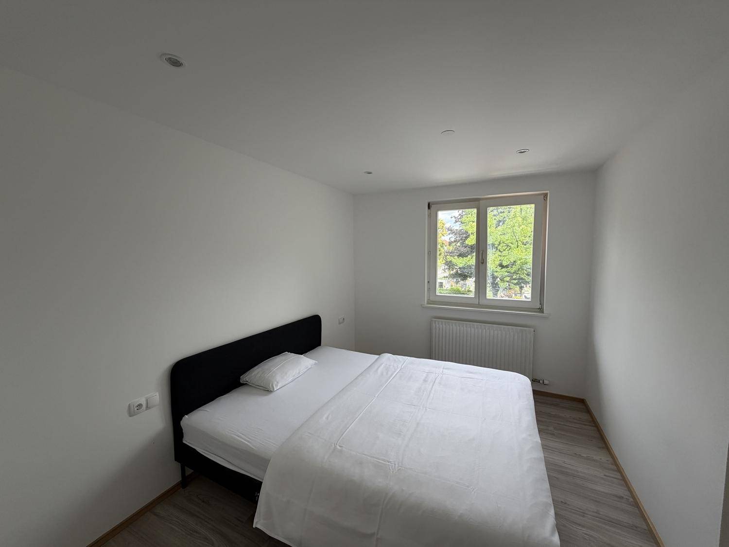 Helles Schlafzimmer mit Doppelbett, Laminatboden und Fenster mit Blick ins Grüne.