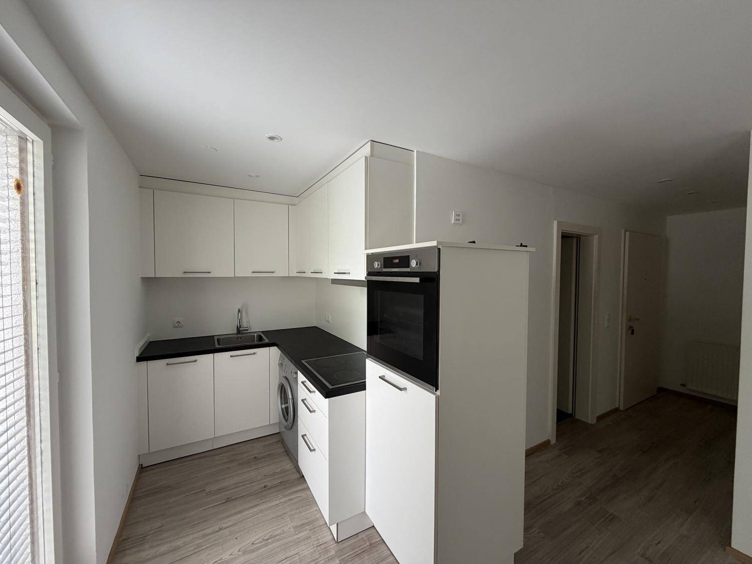 Moderne Küchenzeile mit weißen Schränken, integriertem Backofen und Waschmaschine.