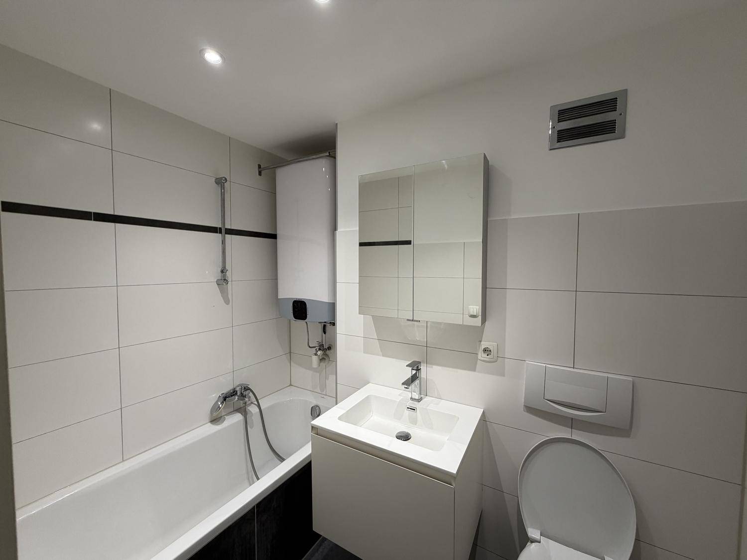 Funktionales Badezimmer mit weißen Fliesen, Badewanne und modernem Waschtisch.