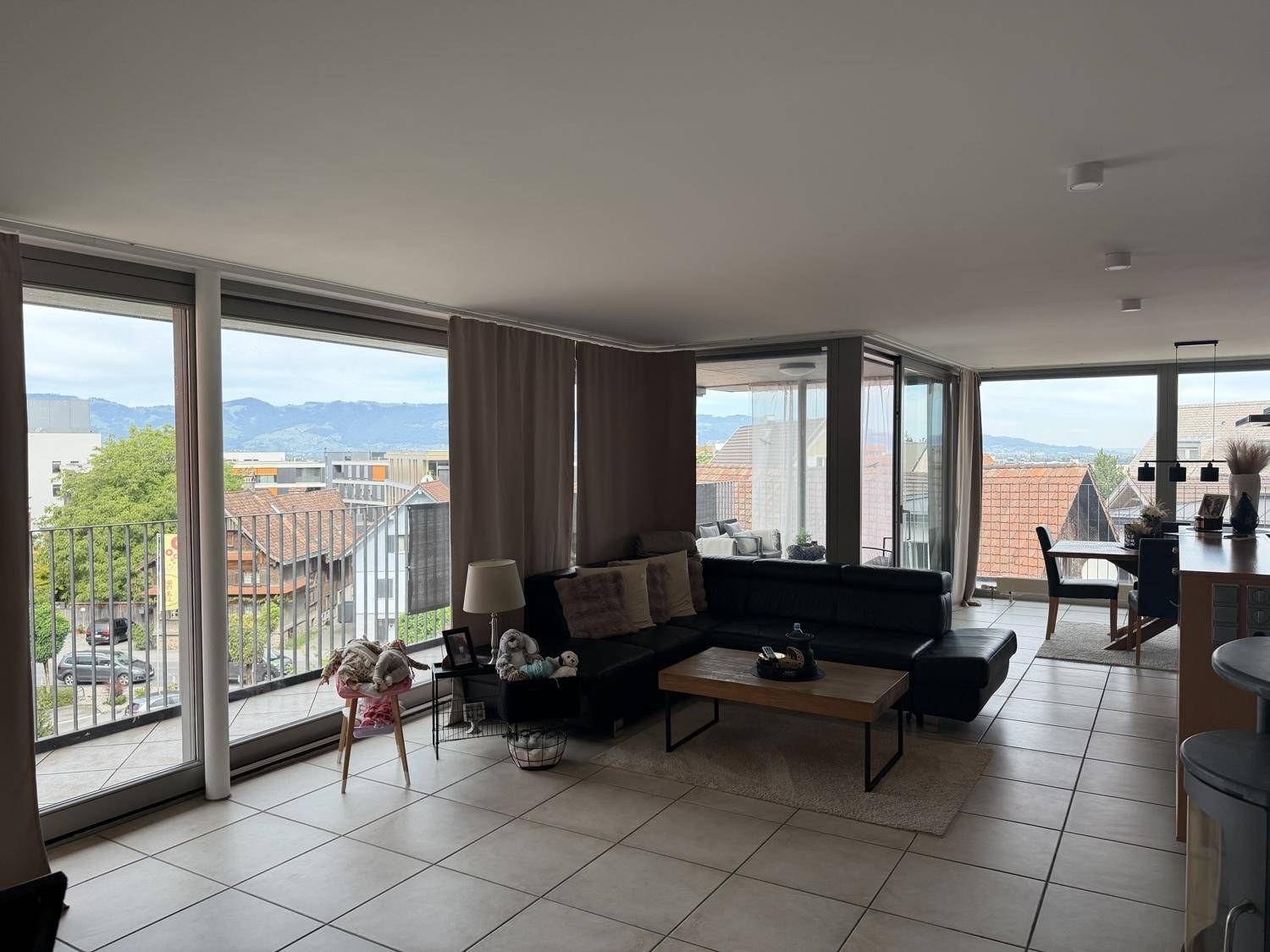 Geräumiges Wohnzimmer mit Ecksofa und großen Fenstern, die einen weiten Blick auf die Stadt und Berge ermöglichen.